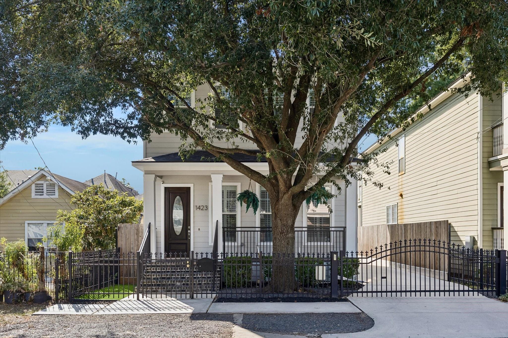 White-sided home behind a black metal gate, shaded by a large front-yard tree.
