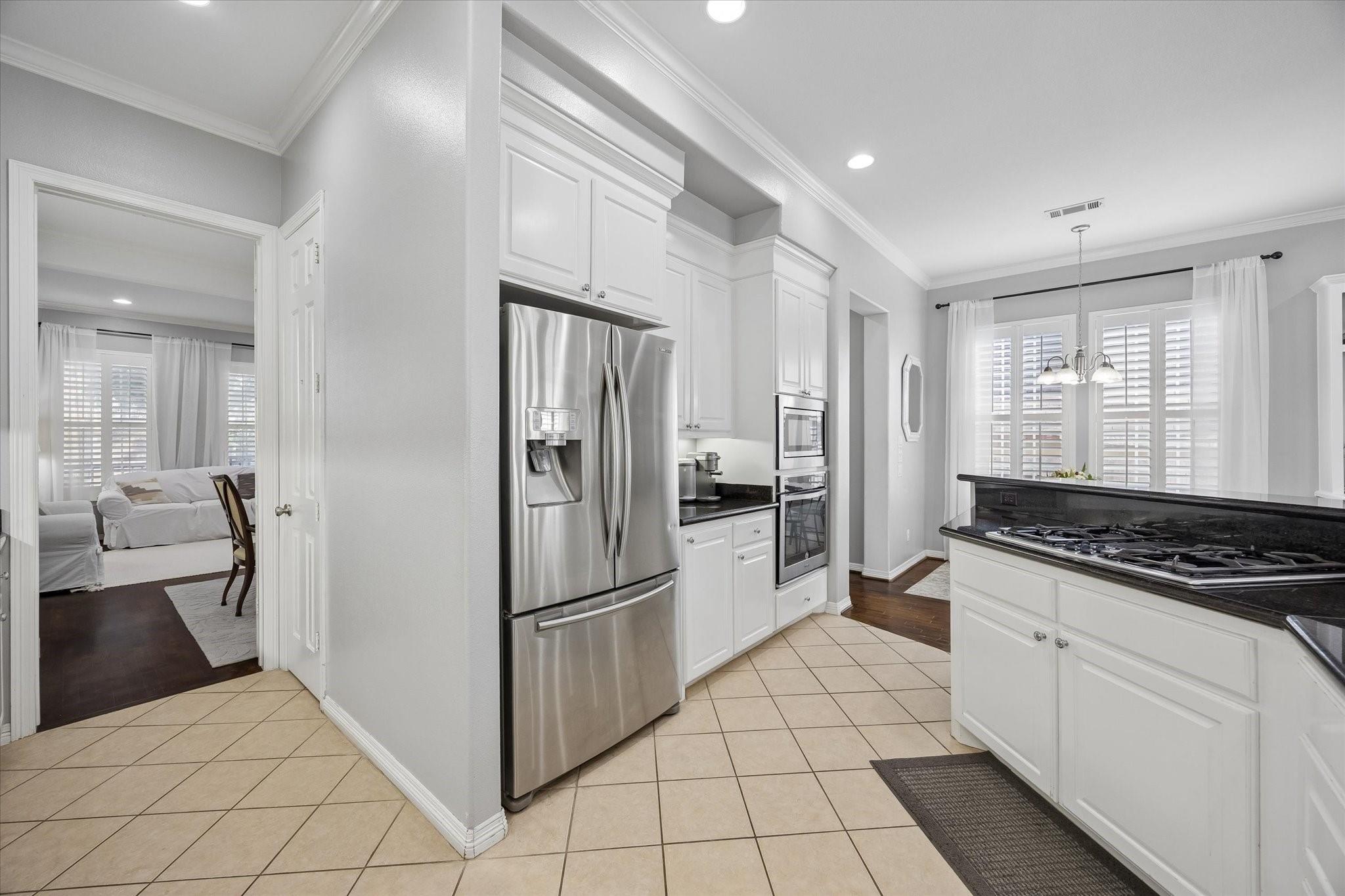 Kitchen with white cabinets, stainless steel appliances, black countertops, and a central cooktop island.