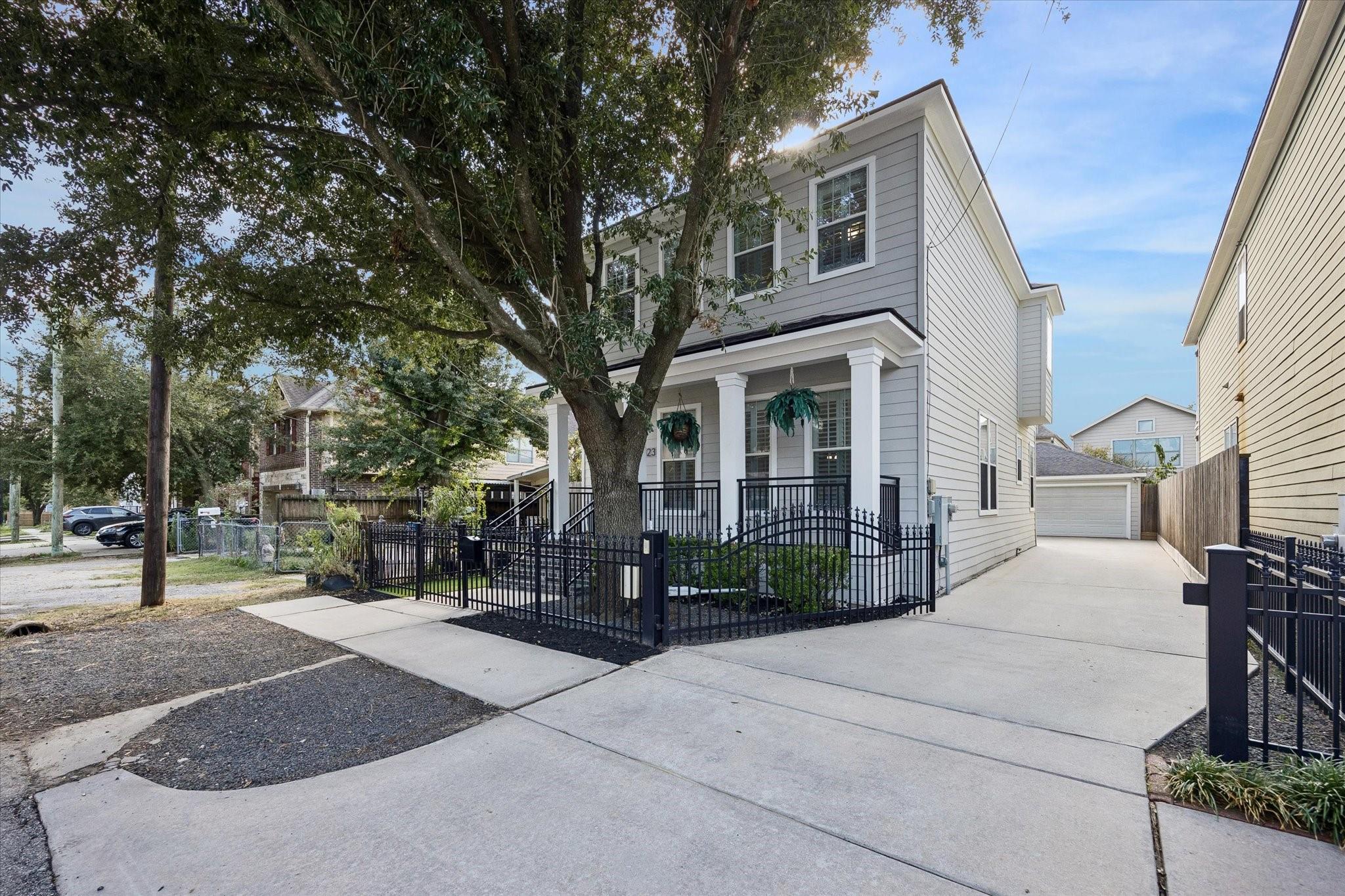 Gray two-story home with a covered porch, black metal fence, and long driveway.