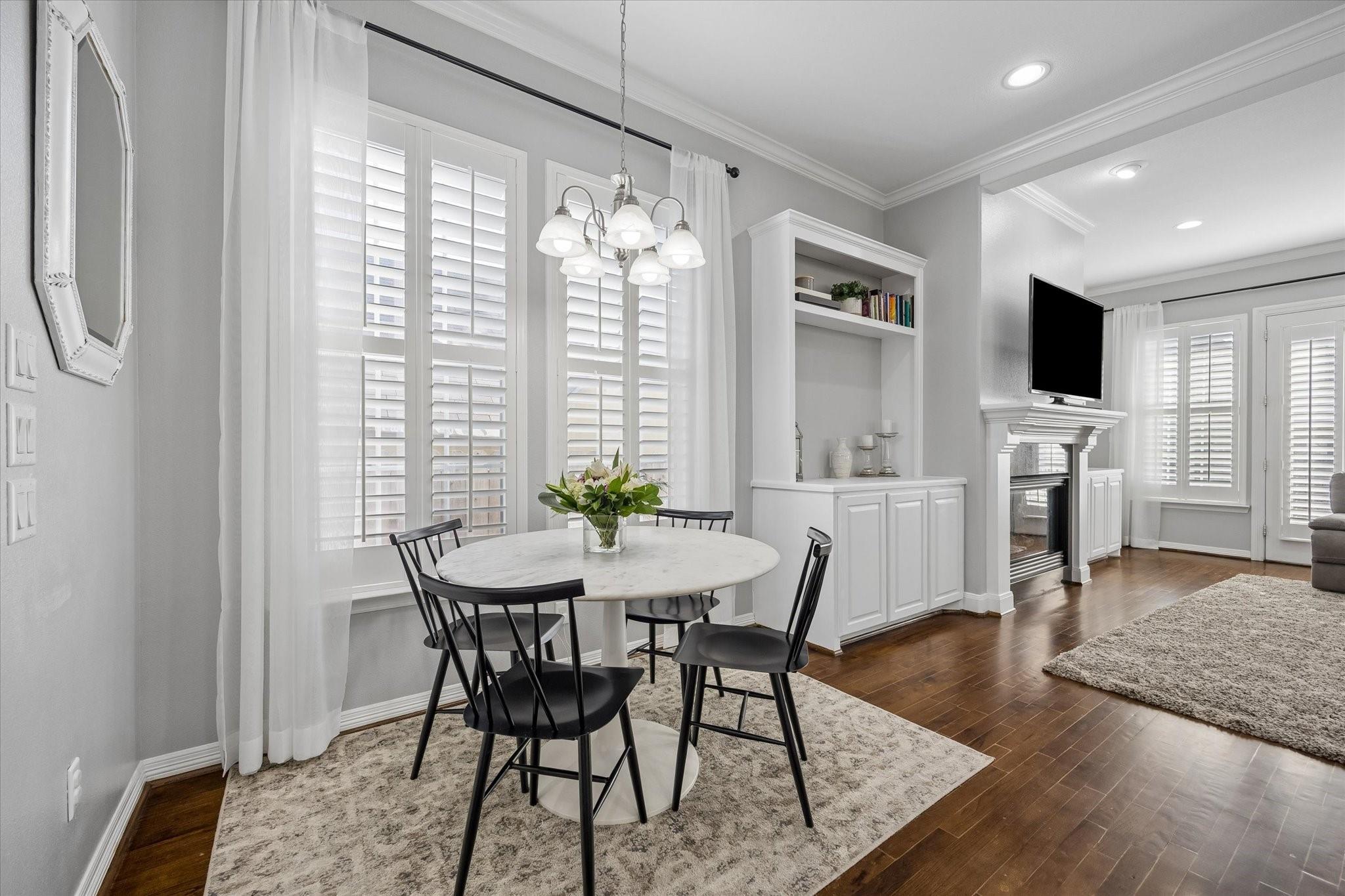 Dining area with a round table, plantation shutters, and built-in shelving beside the living room.