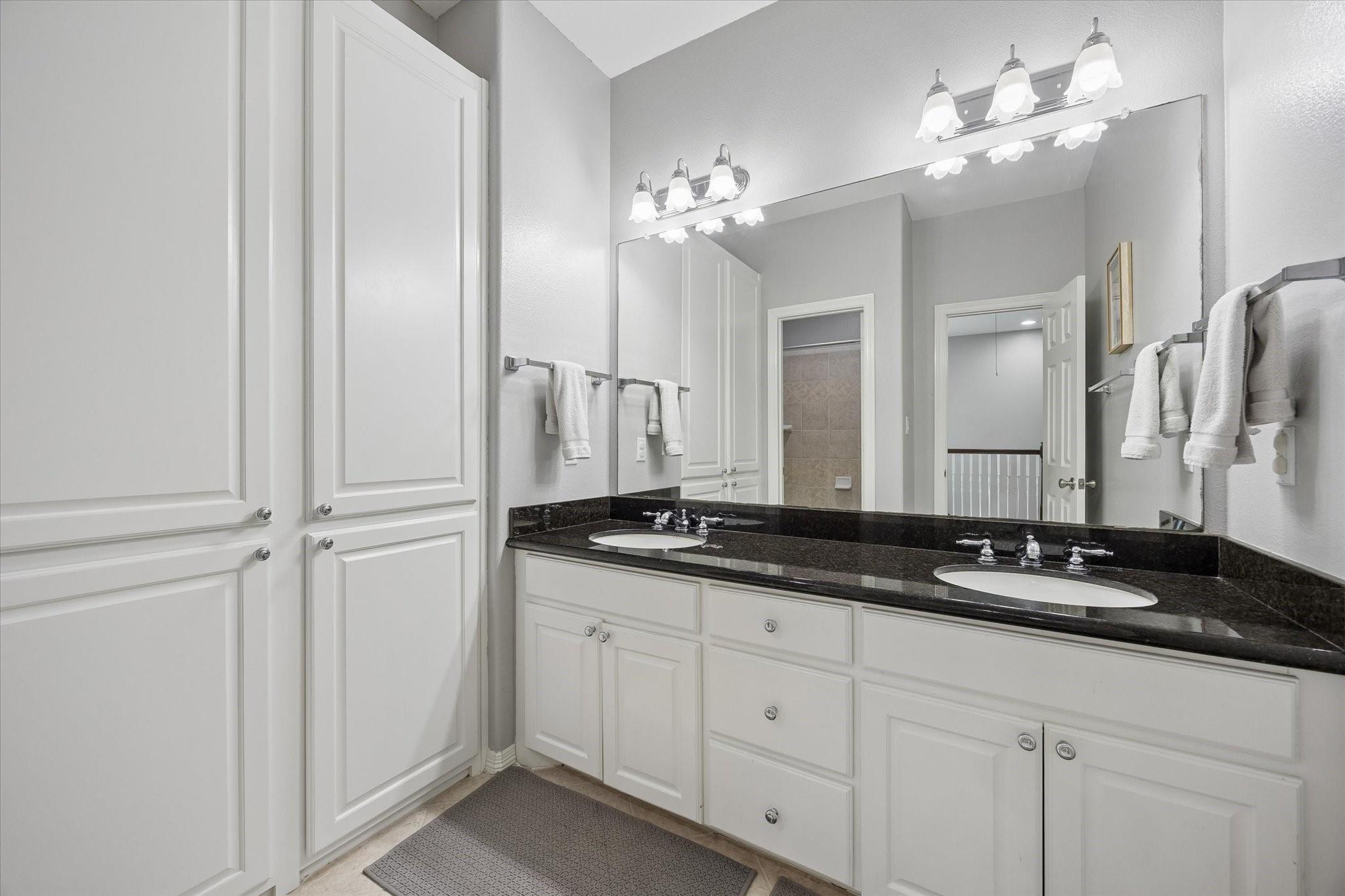 Bathroom vanity with double sinks, dark countertop, large mirror, and white cabinetry.