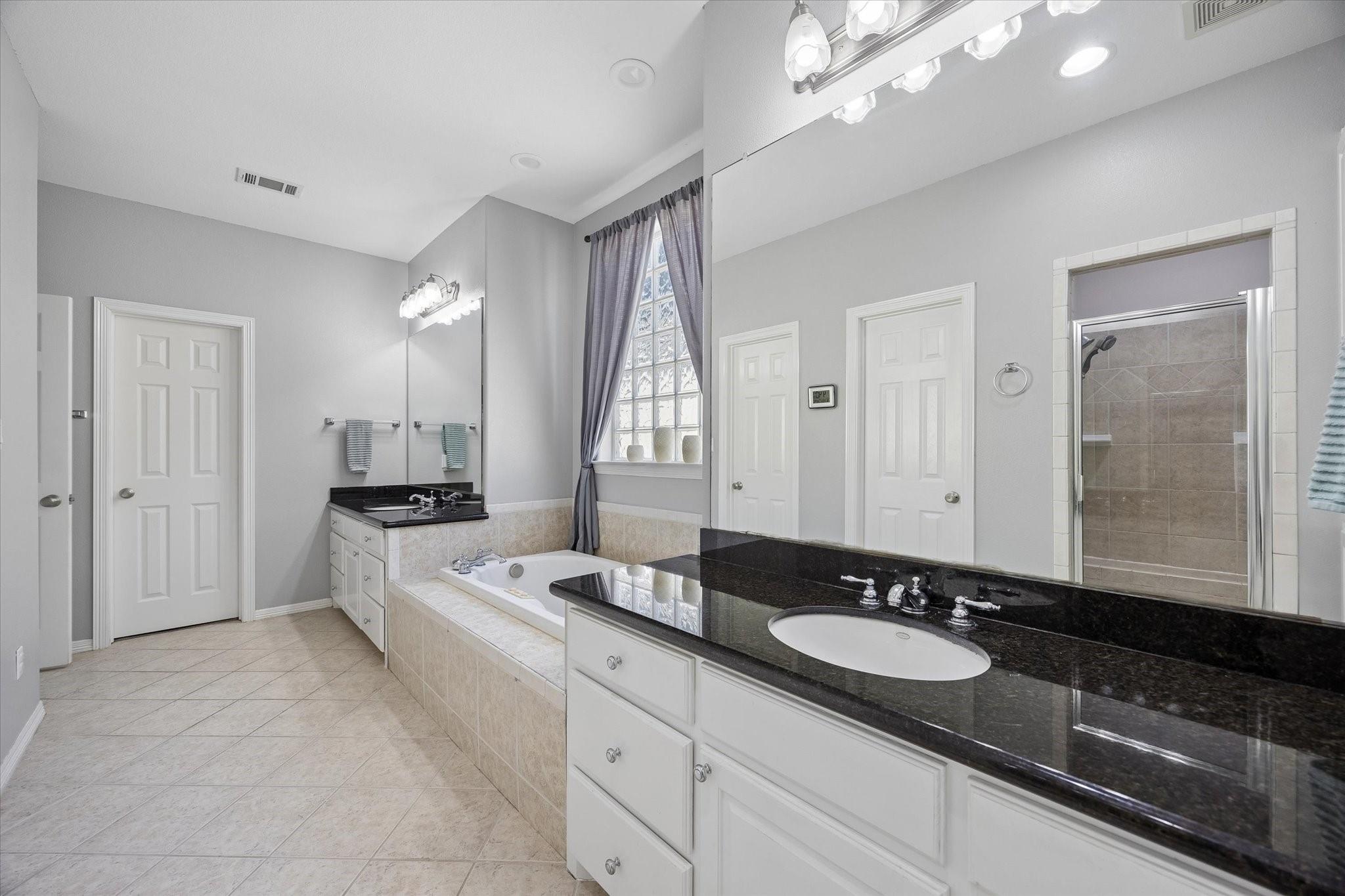 Bathroom with a double vanity, soaking tub, and glass-block window.