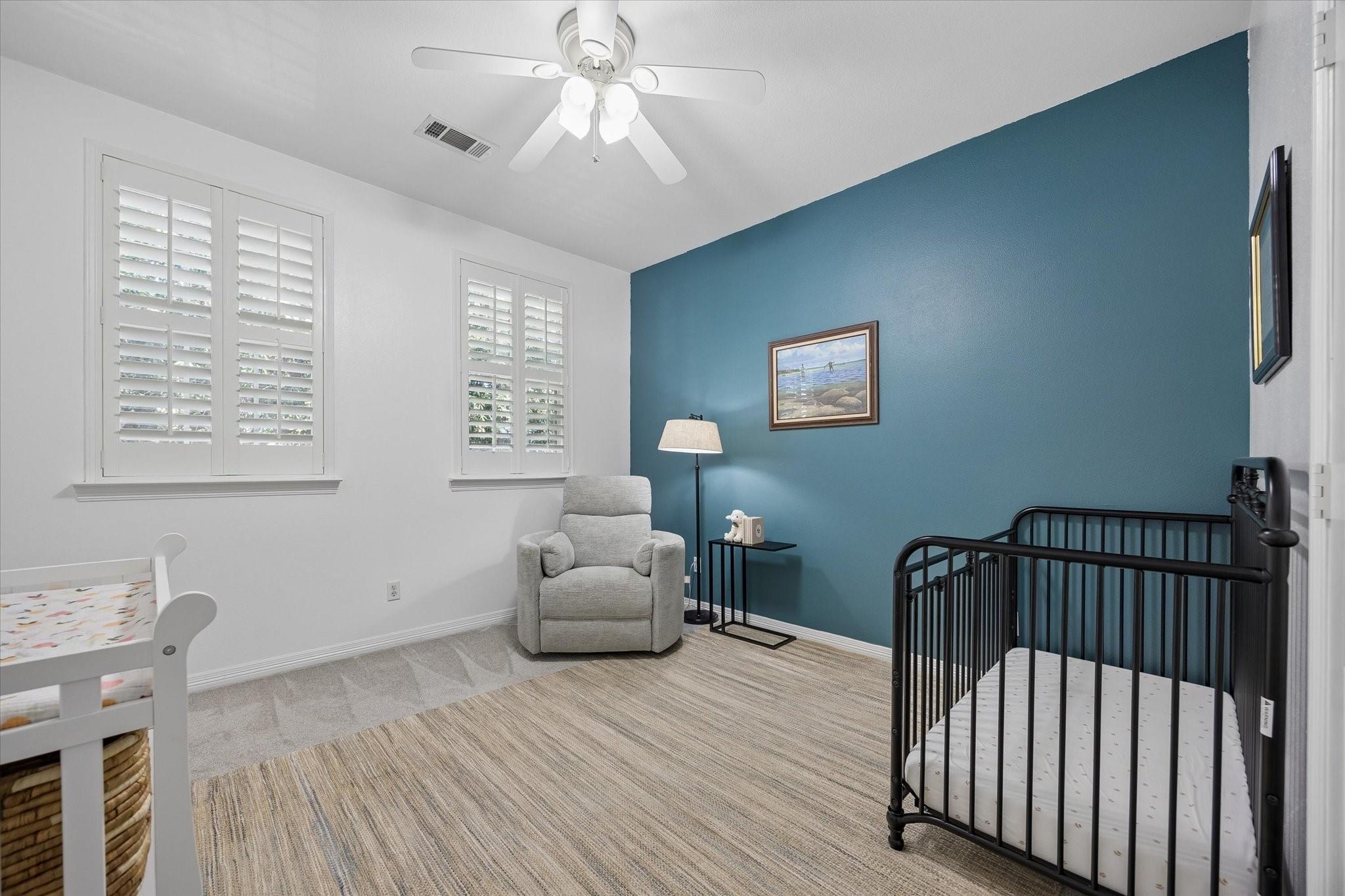 Bedroom with a teal accent wall, black crib, white toddler bed, and gray armchair.