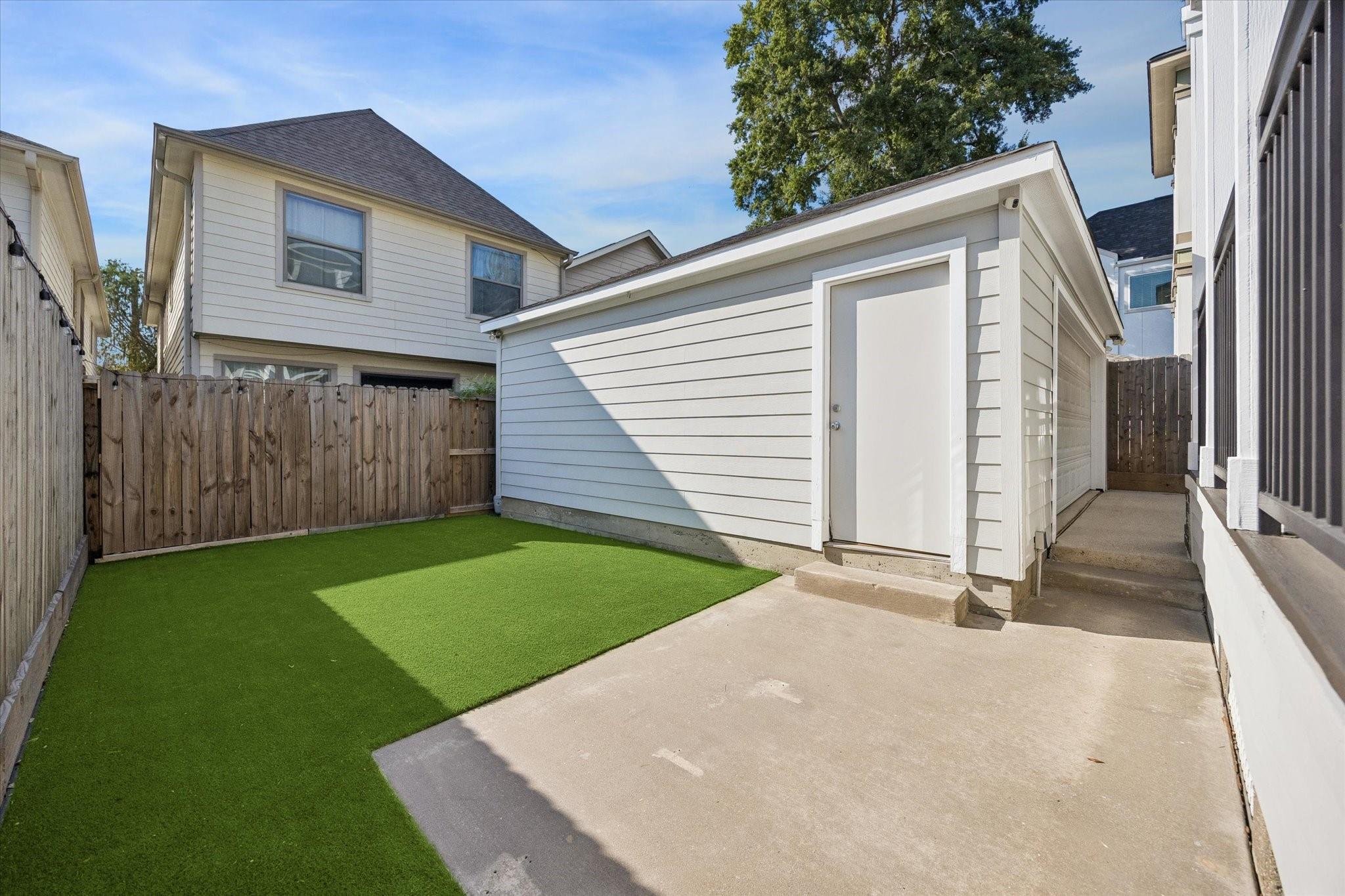 Fenced backyard with artificial turf, a concrete patio, and a white-sided garage.