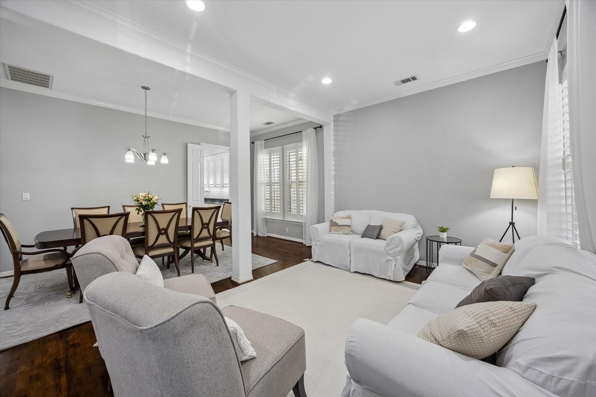 Open living and dining room with white sofas, a dark wood dining table, and plantation-shuttered windows.