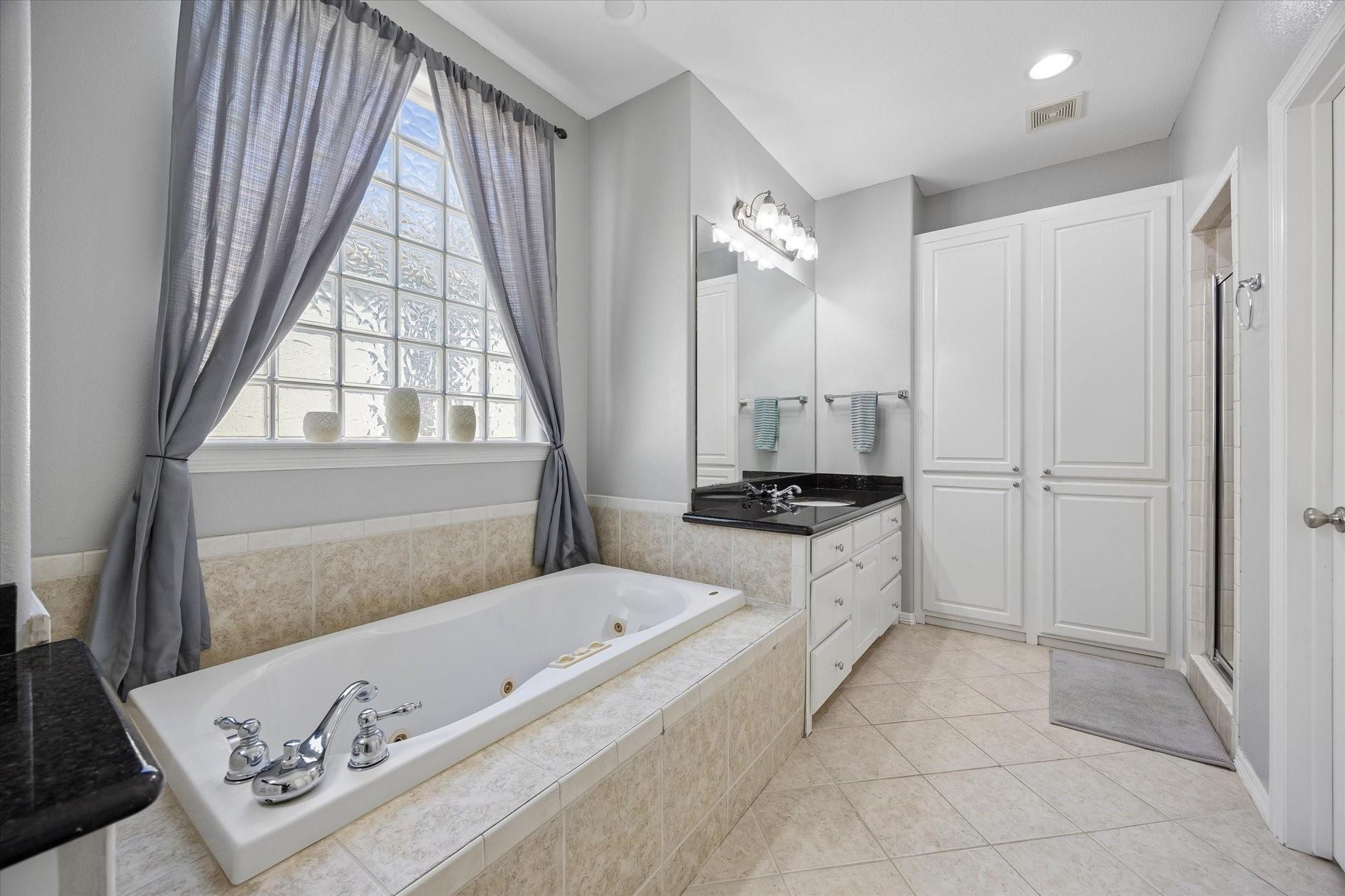 Bathroom with a jetted tub beneath a glass-block window and a double-sink vanity.