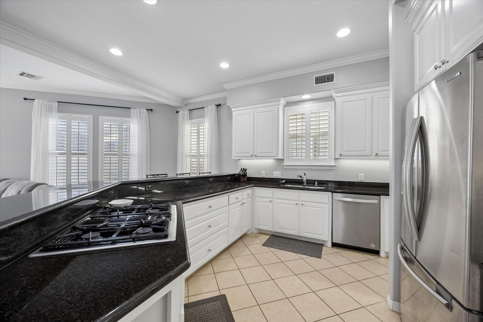 Kitchen with white cabinets, black granite counters, gas cooktop, and stainless steel appliances.