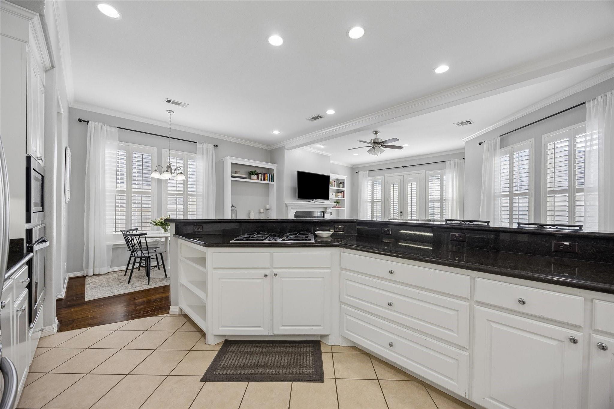 Kitchen with white cabinetry, black granite counters, gas cooktop, and adjoining dining nook.