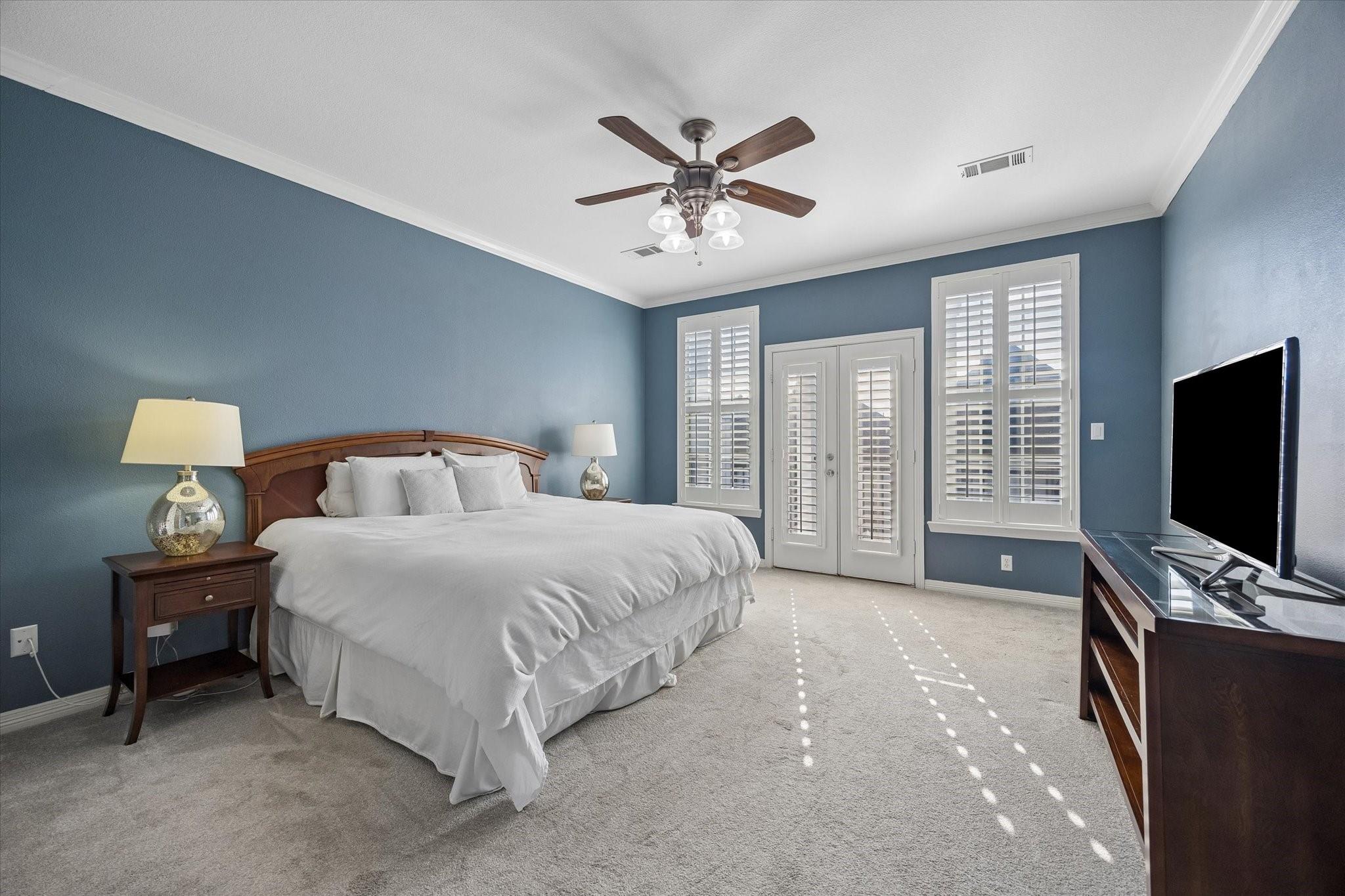 Furnished bedroom with blue walls, a large bed, plantation shutters, and French doors.