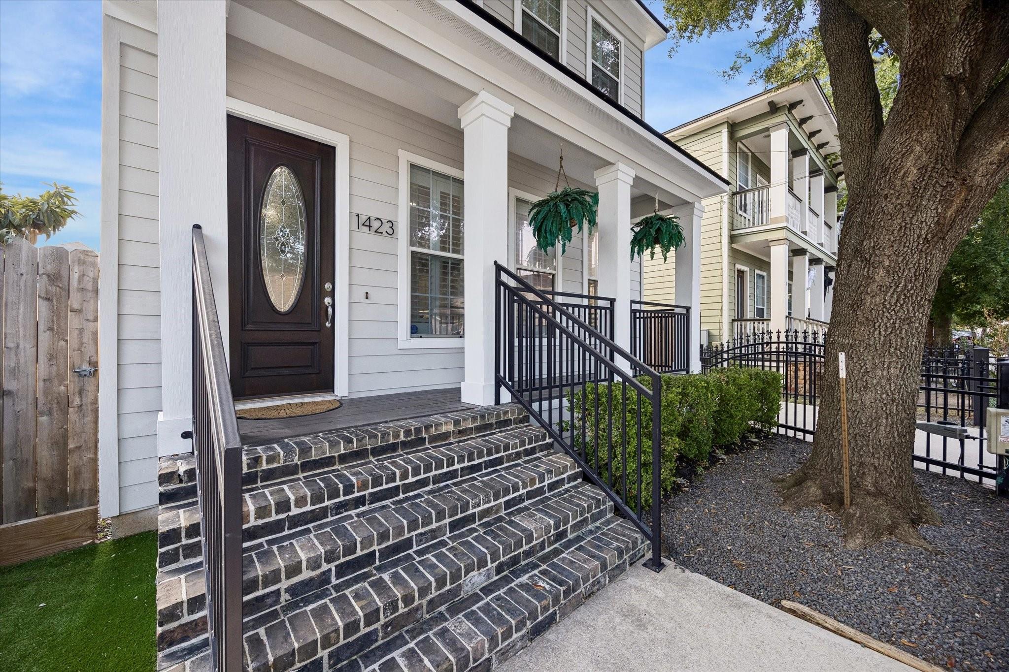 Front porch with broad brick steps, white columns, hanging ferns, and a dark oval-glass door.