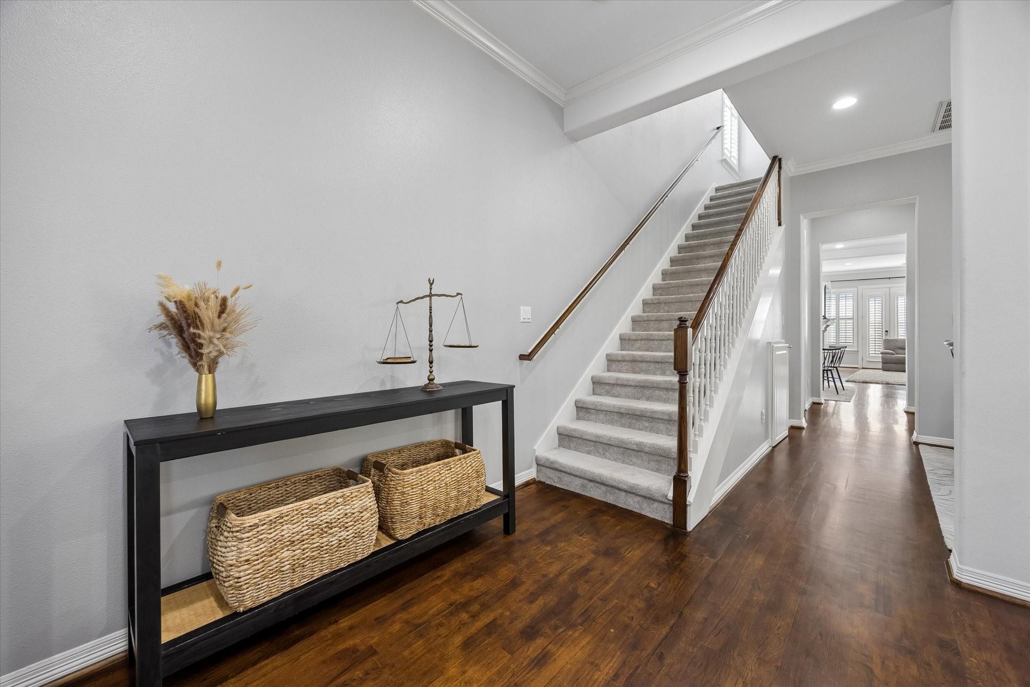 Entry foyer with carpeted staircase, dark wood floors, and console table with woven baskets.