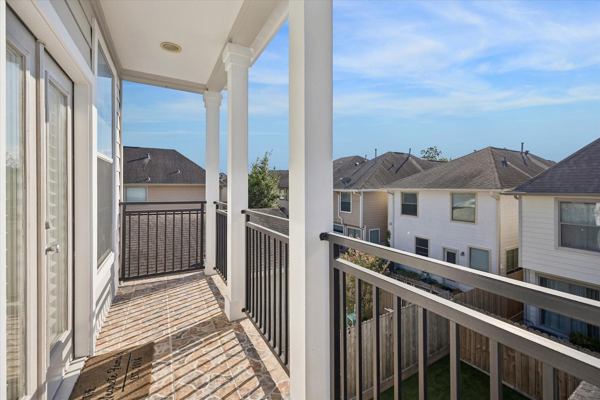 Covered upper-level balcony with tiled flooring and black metal railings overlooking neighboring homes.