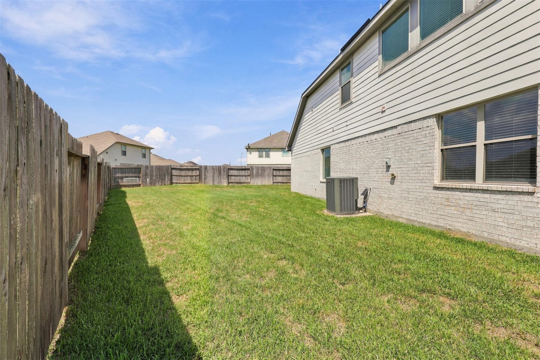 Fenced backyard with a green lawn beside the home's brick-and-siding exterior.