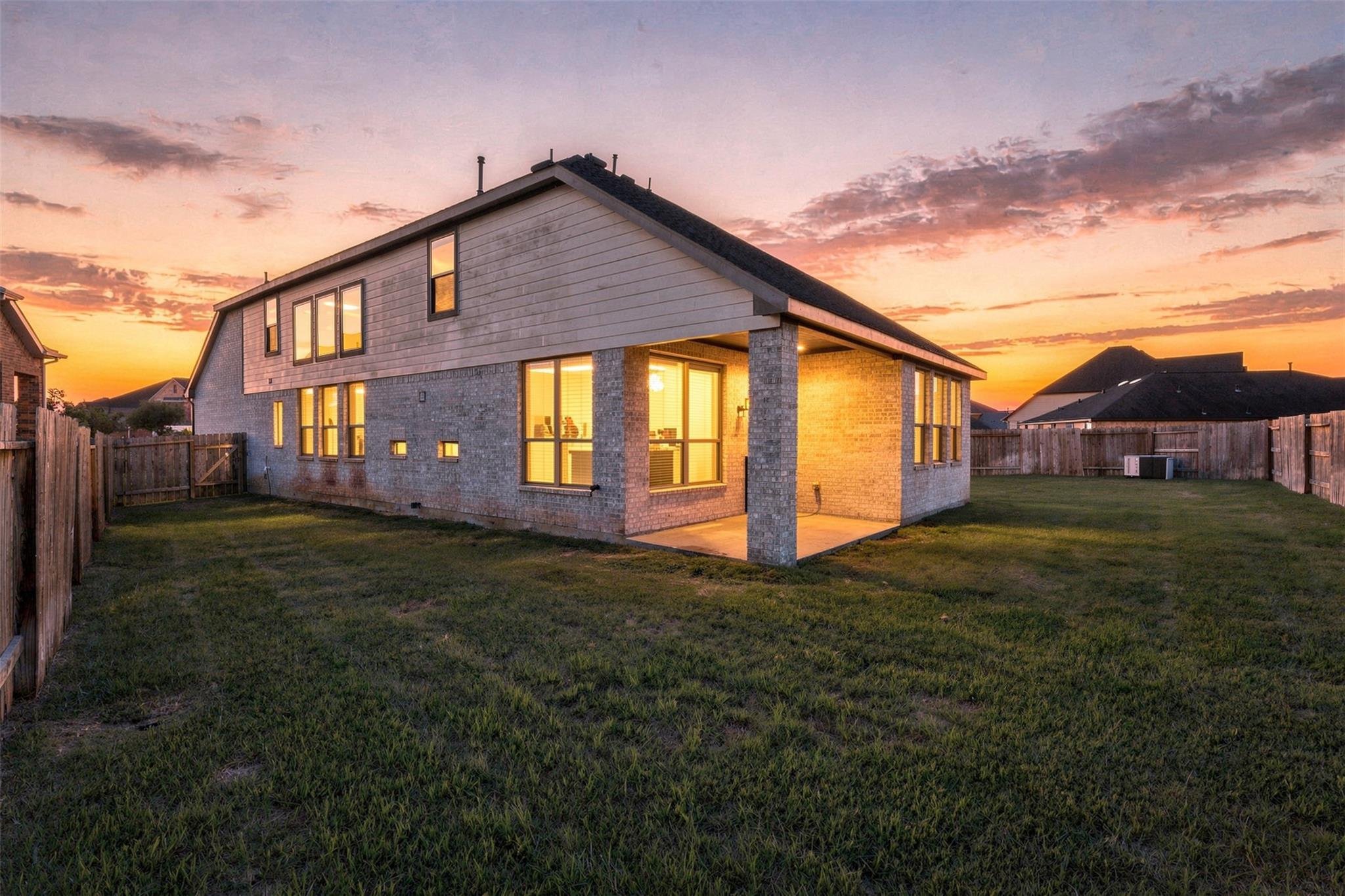 Two-story home with a covered patio and fenced backyard glowing at sunset.