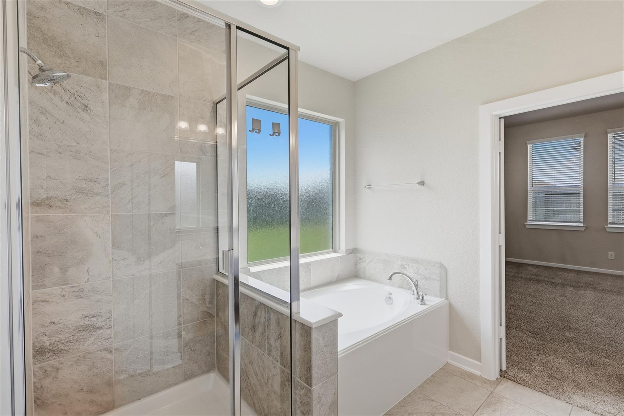 Bathroom with a glass-enclosed tiled shower, soaking tub, and frosted window.