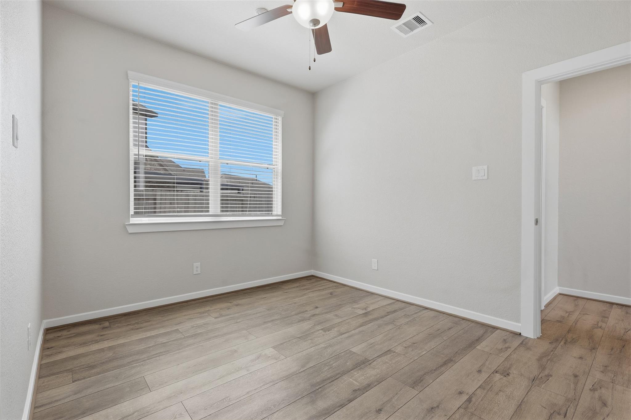 Empty room with wood-look flooring, a window with blinds, and a ceiling fan.