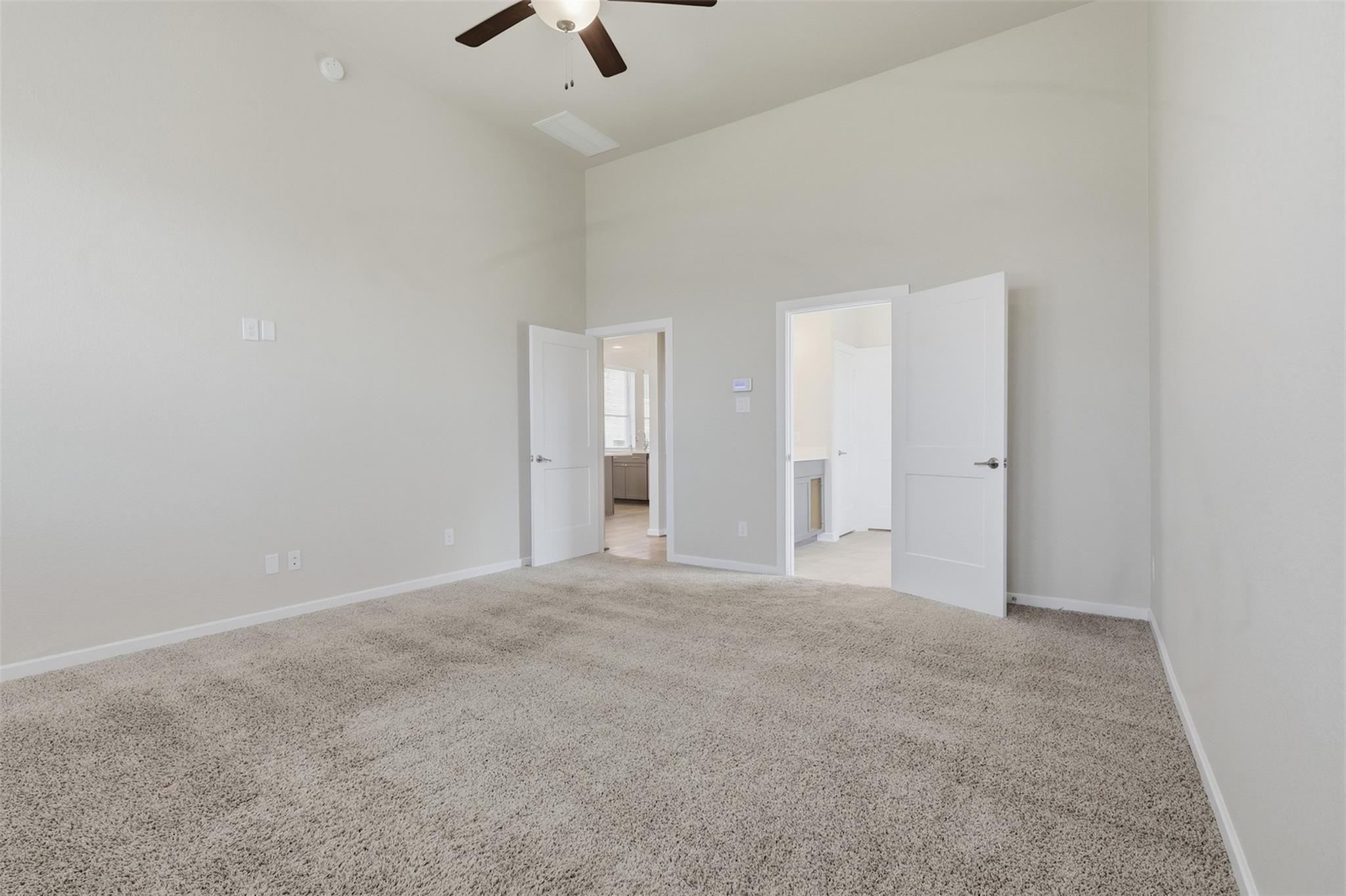 Empty carpeted bedroom with a ceiling fan and two open doorways.