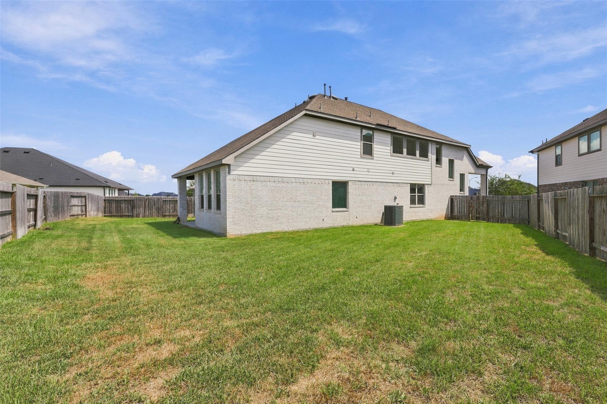 Two-story house viewed from its fenced backyard, with a broad grassy lawn and neighboring homes.