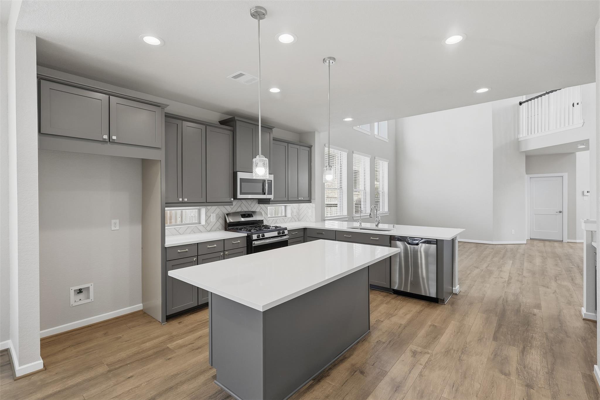Modern kitchen with gray cabinetry, a large white island, and stainless steel appliances.