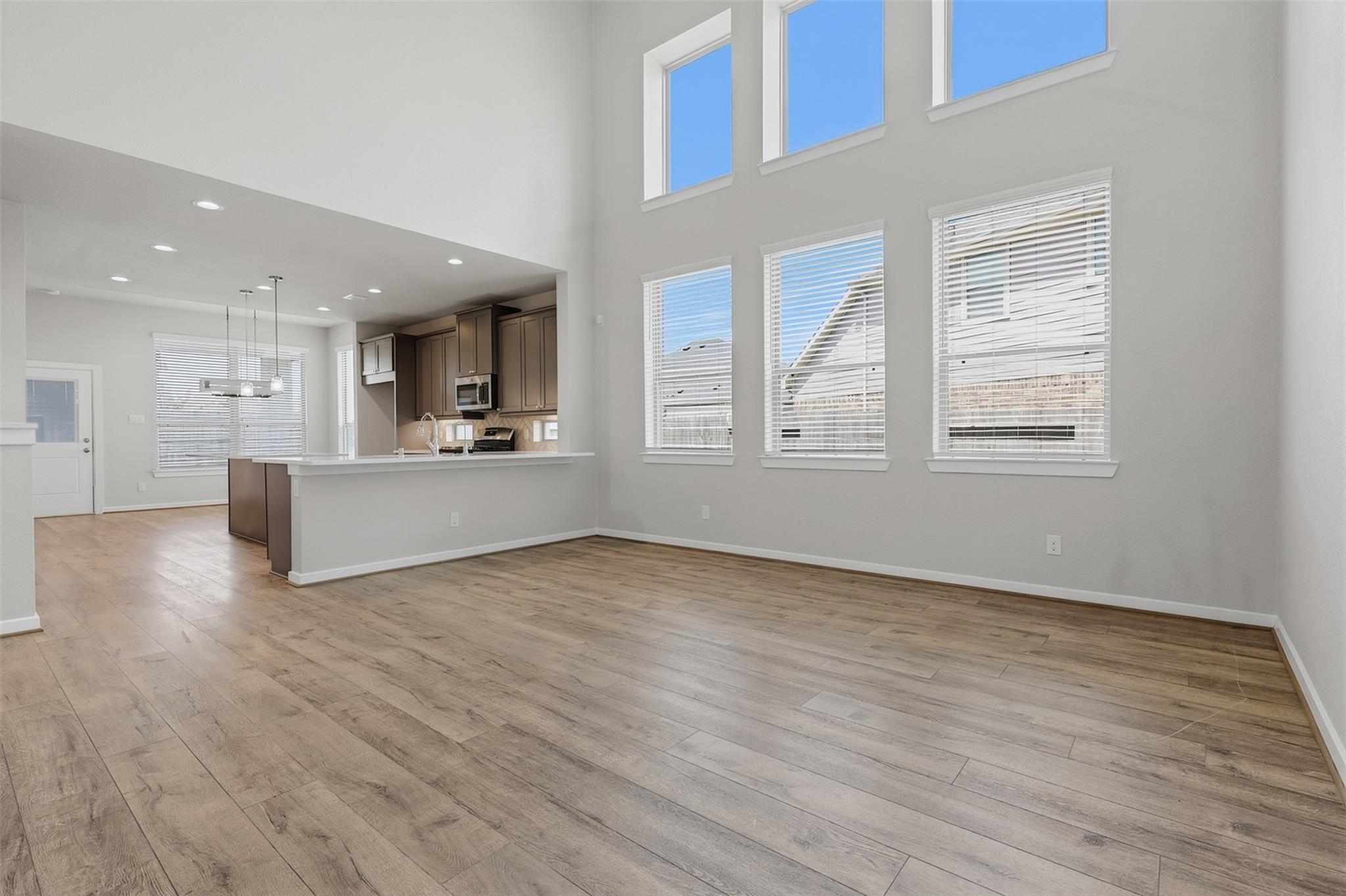 Vacant open-plan living area with tall windows, wood-look floors, and a kitchen breakfast bar.