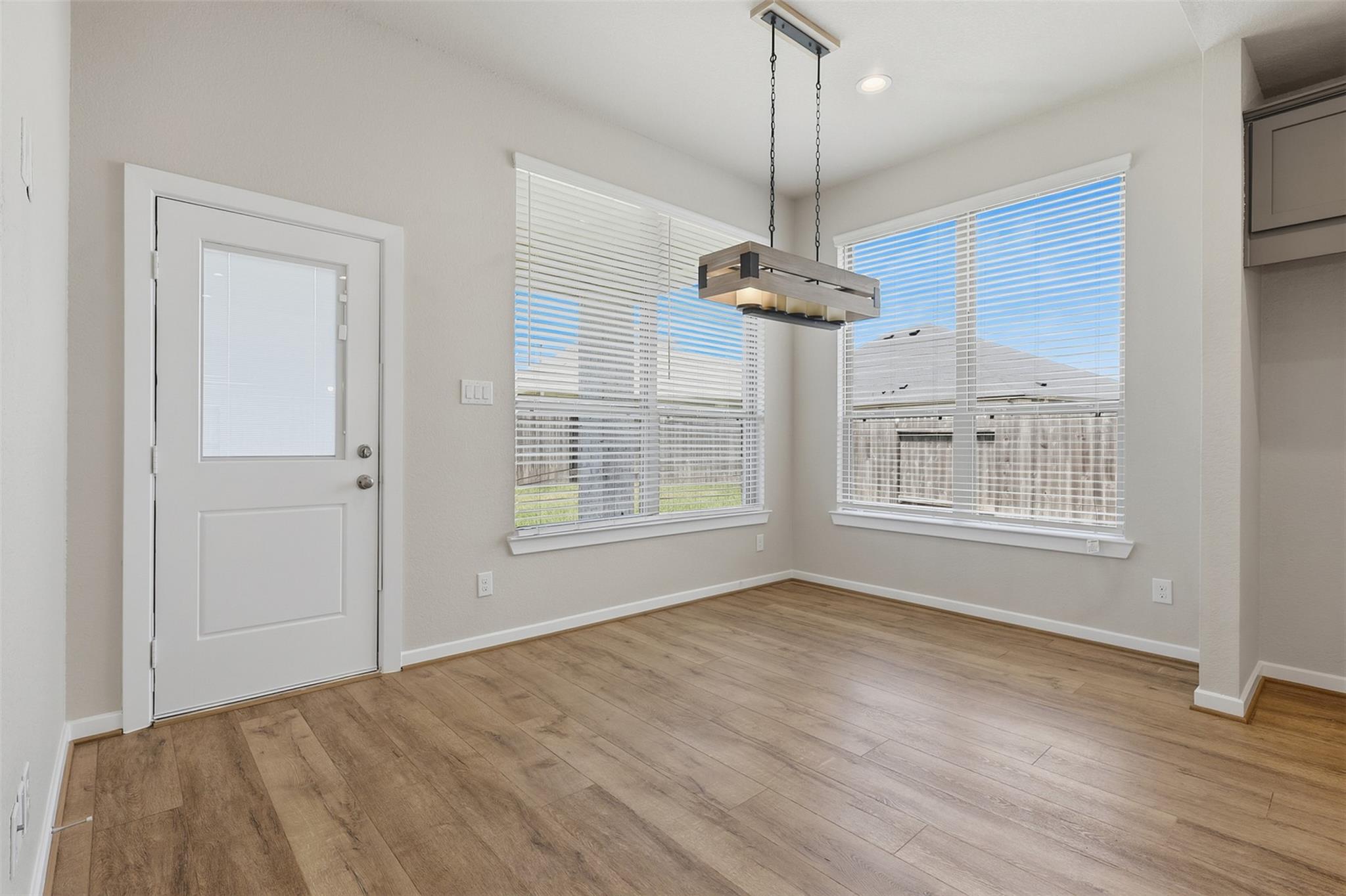 Empty dining area with wood-look flooring, two large blinded windows, and a rectangular pendant light.