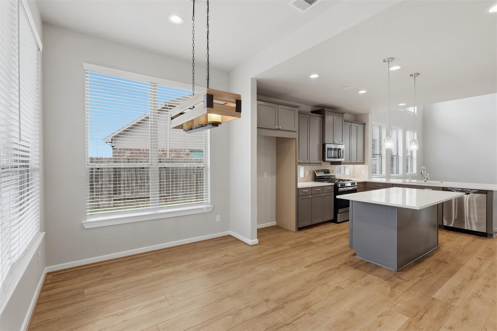 Open-plan kitchen and dining area with a white island, gray cabinets, and wood-look floors.