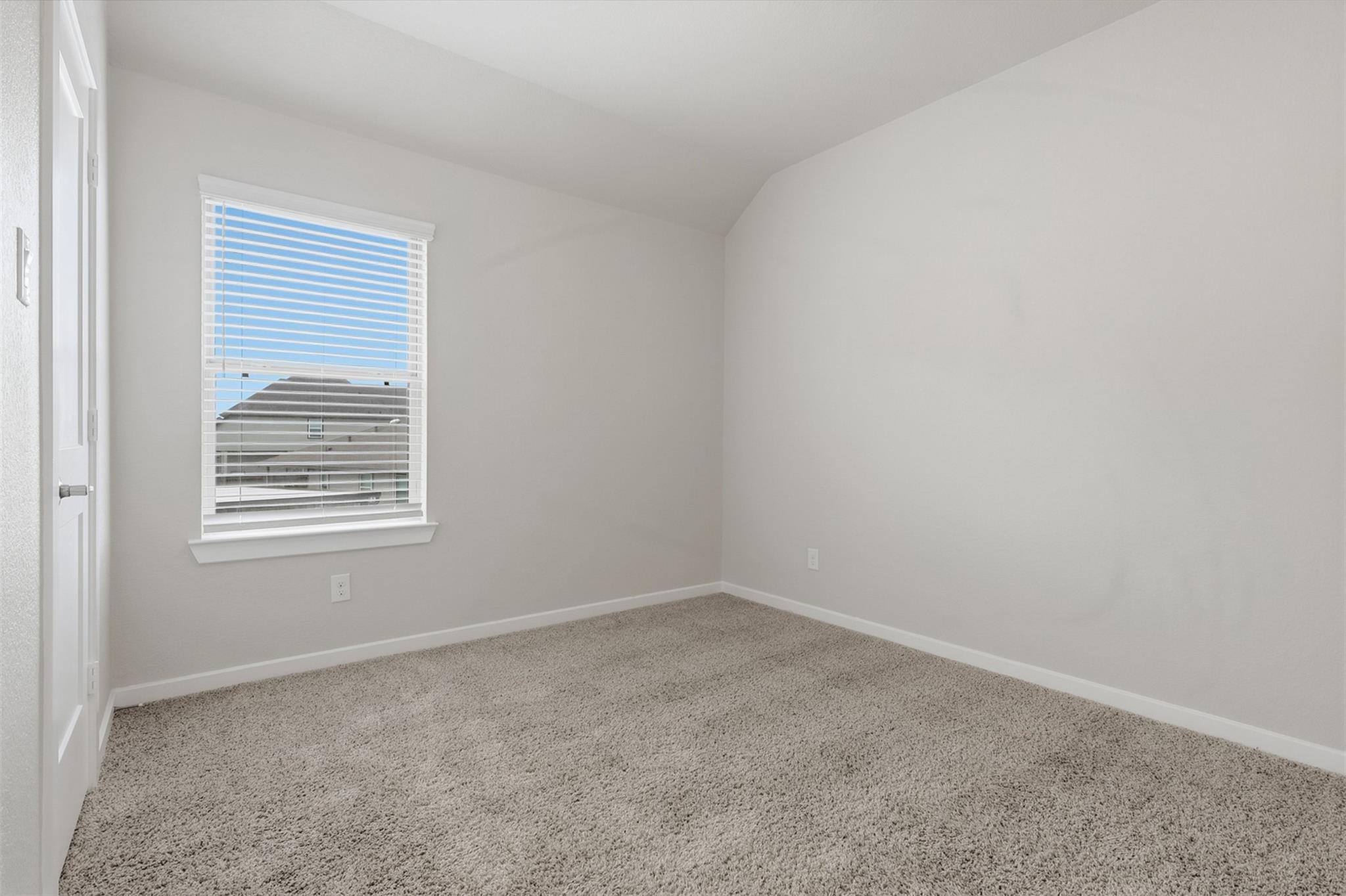 Empty carpeted room with a window fitted with white blinds.