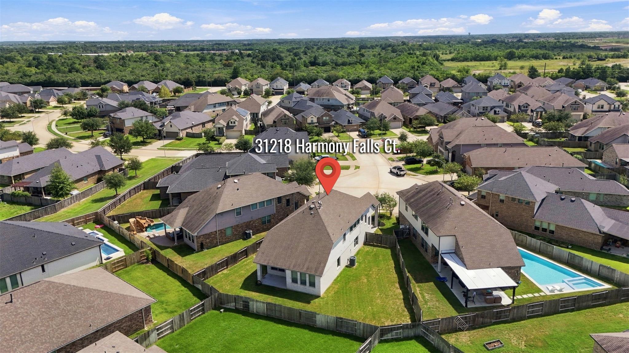 Aerial view of a home marked by a red pin among neighborhood houses, fenced yards, and swimming pools.