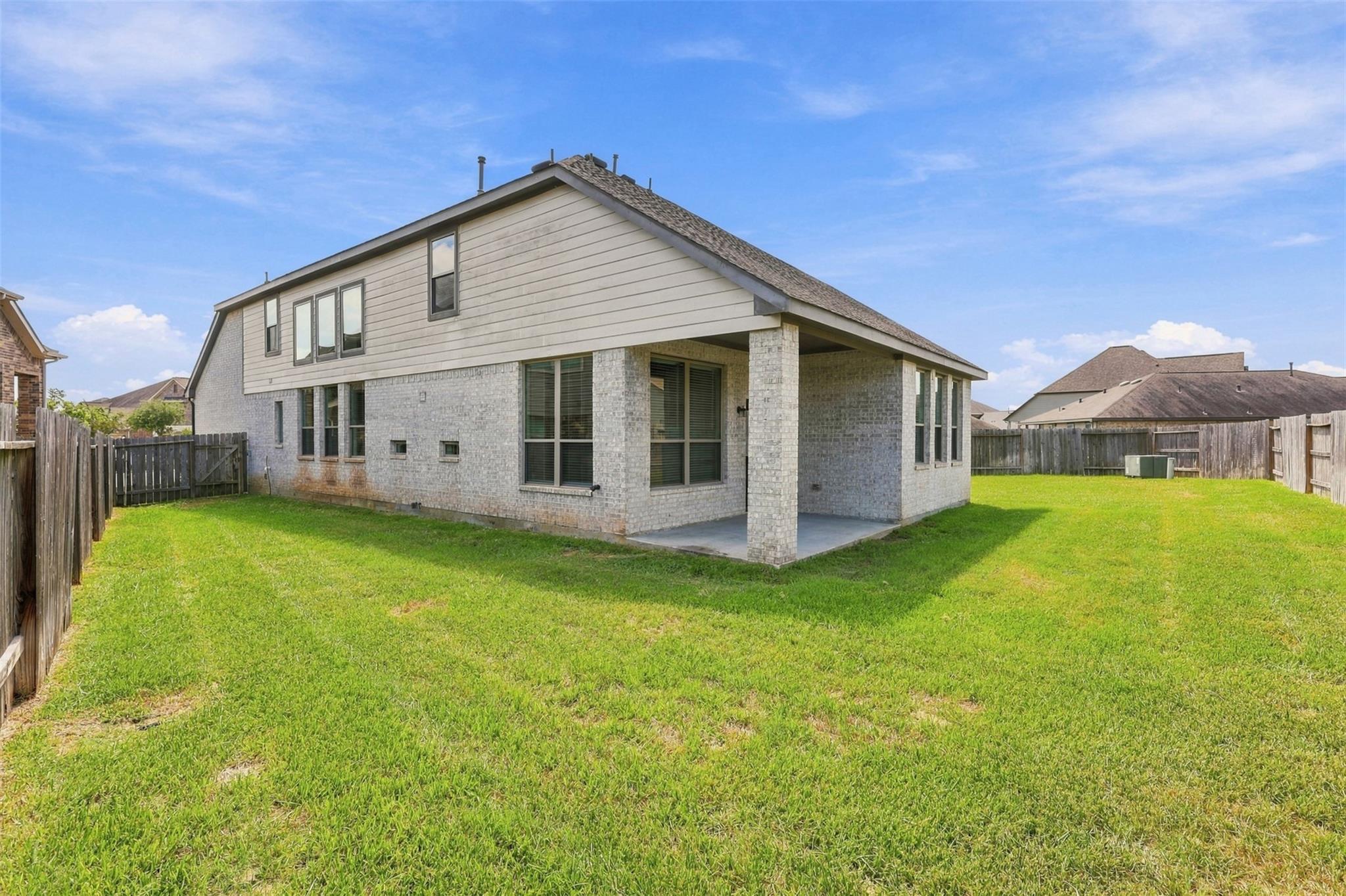 Two-story home with a covered patio overlooking a large fenced grassy backyard.