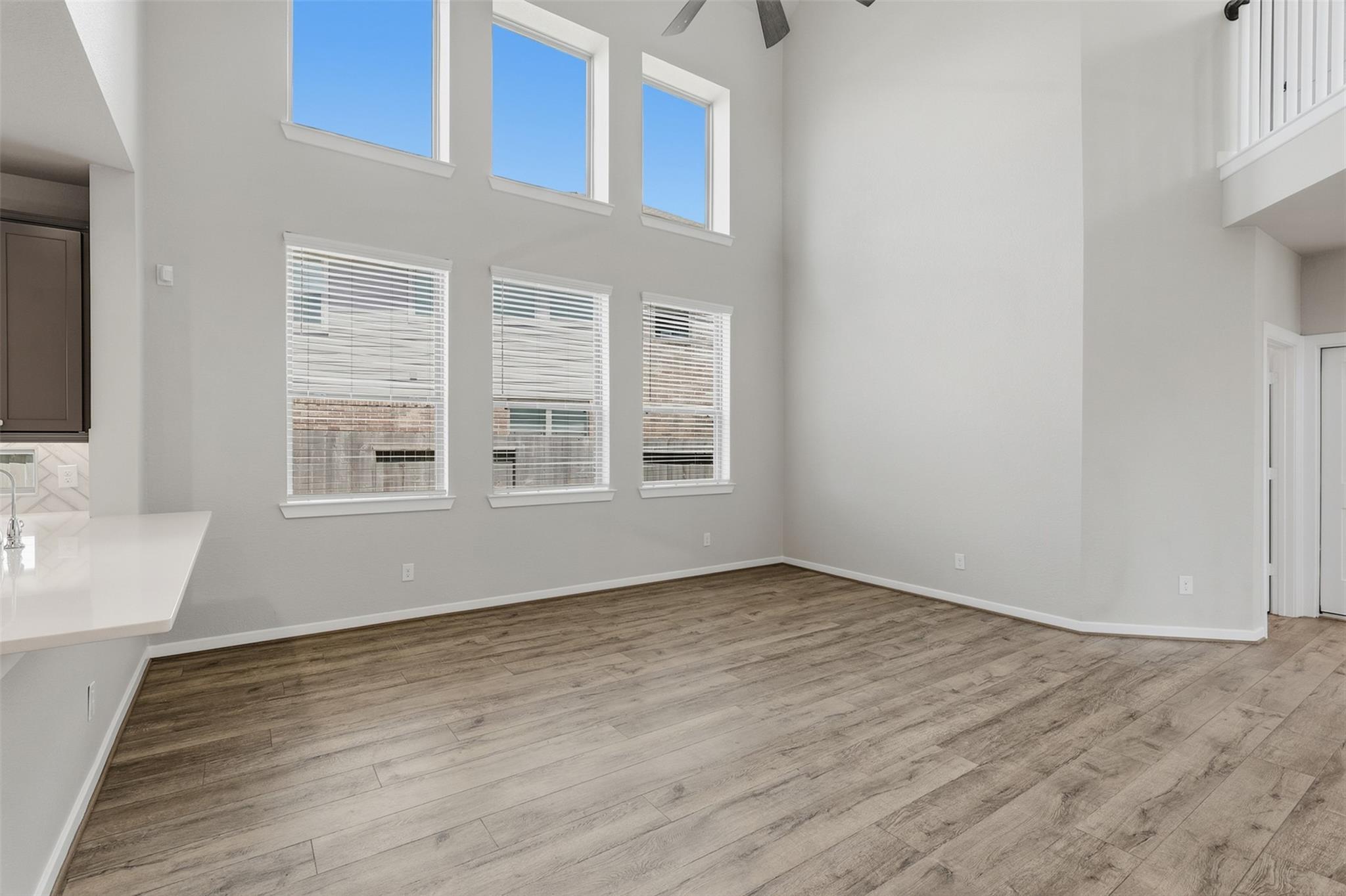 Vacant double-height living room with wood-look floors and tall windows.