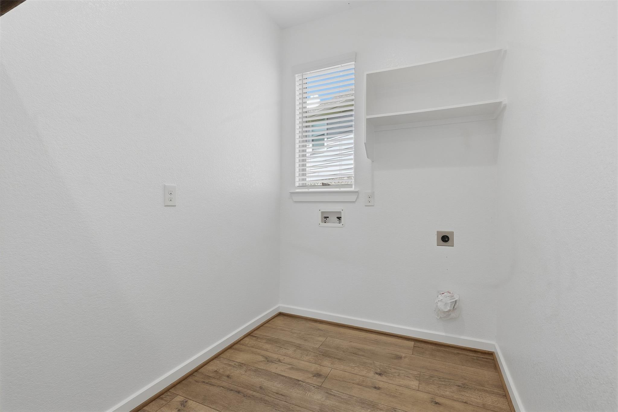 Empty laundry room with washer and dryer hookups, a window, and a wall shelf.