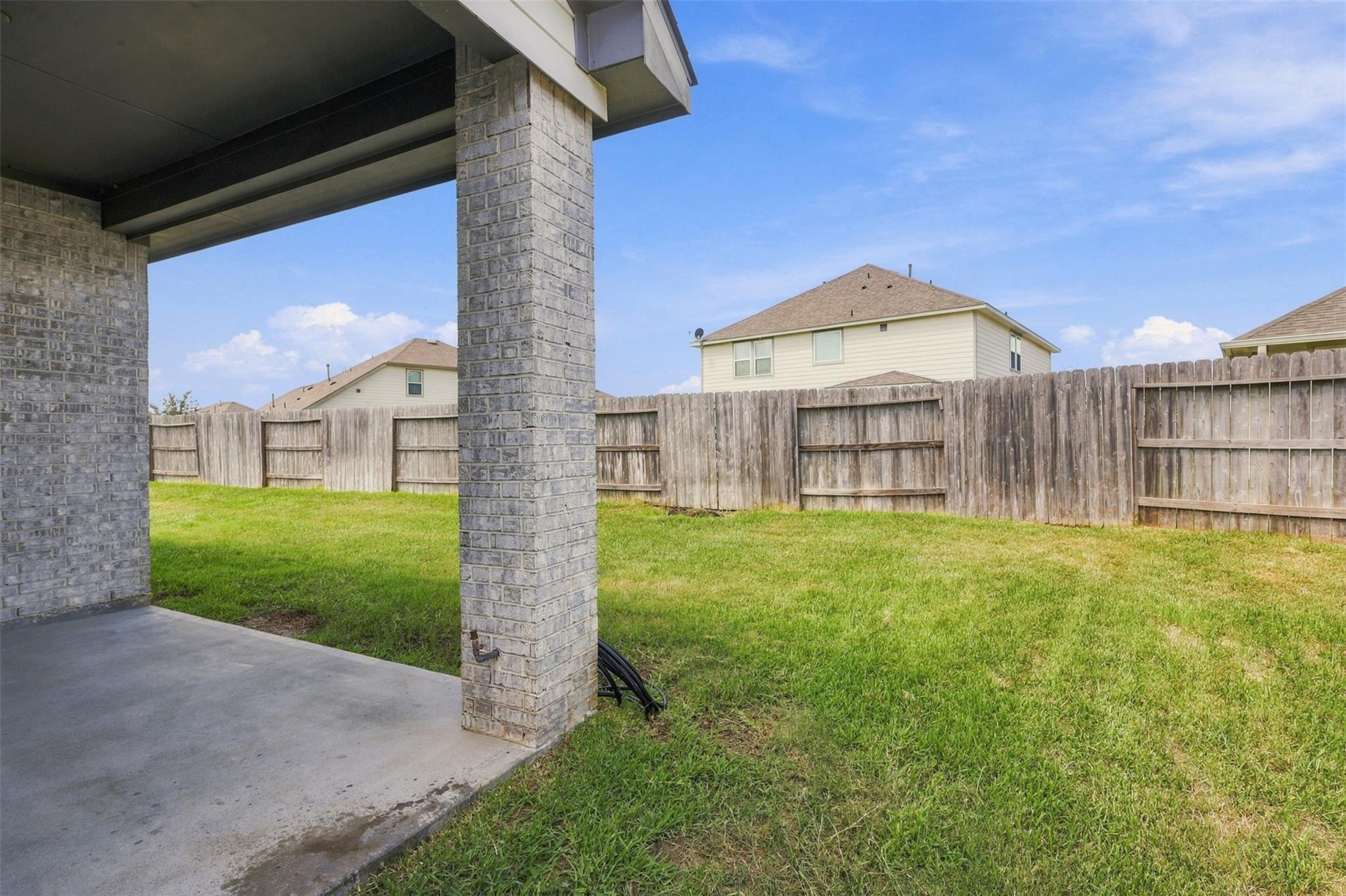 Backyard lawn and wooden privacy fence seen from a covered patio with brick columns.