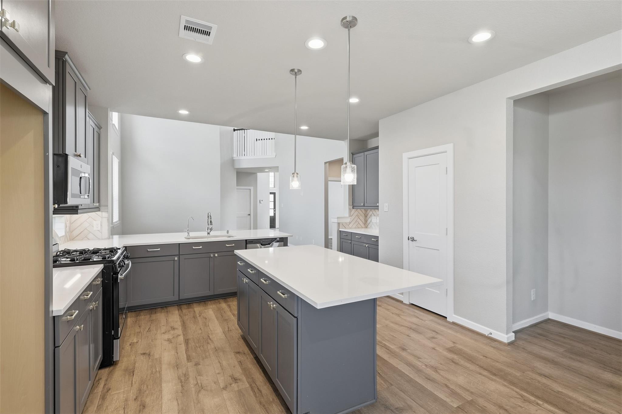 Open kitchen with gray cabinets, two white countertop islands, a gas range, and wood-look floors.