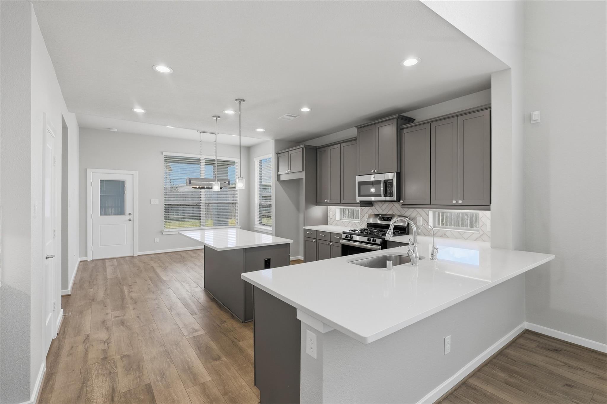 Vacant kitchen with gray cabinets, white island countertop, stainless steel appliances, and wood-look flooring.