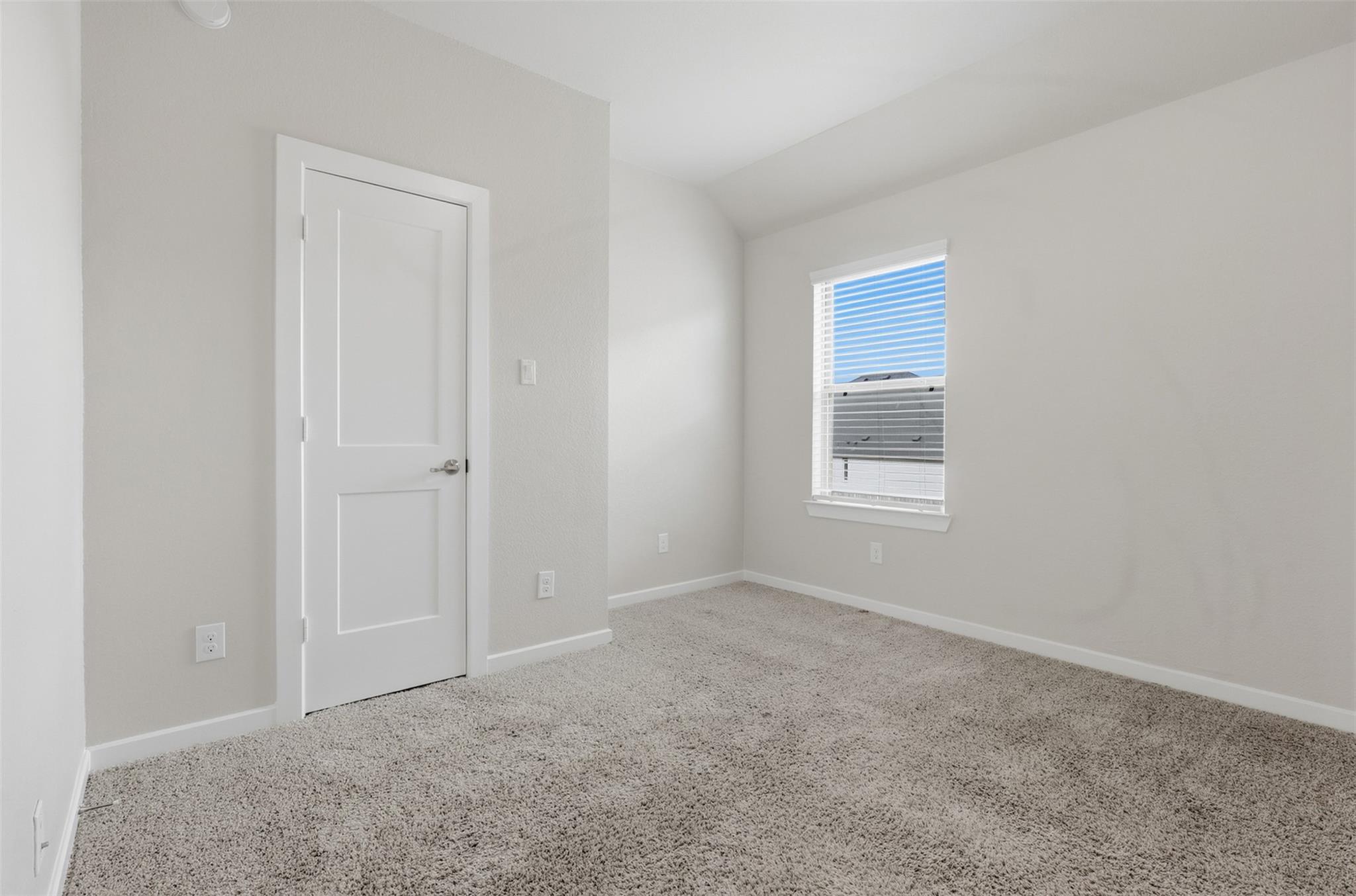 Empty bedroom with beige carpet, a white paneled door, and a window with blinds.