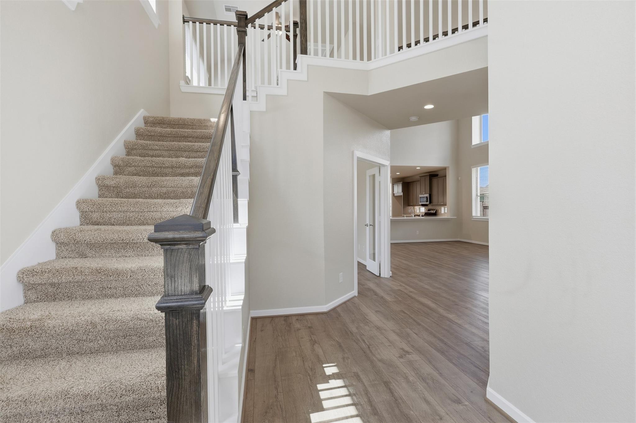 Carpeted staircase with dark wood handrail beside an open entry and wood-look flooring.