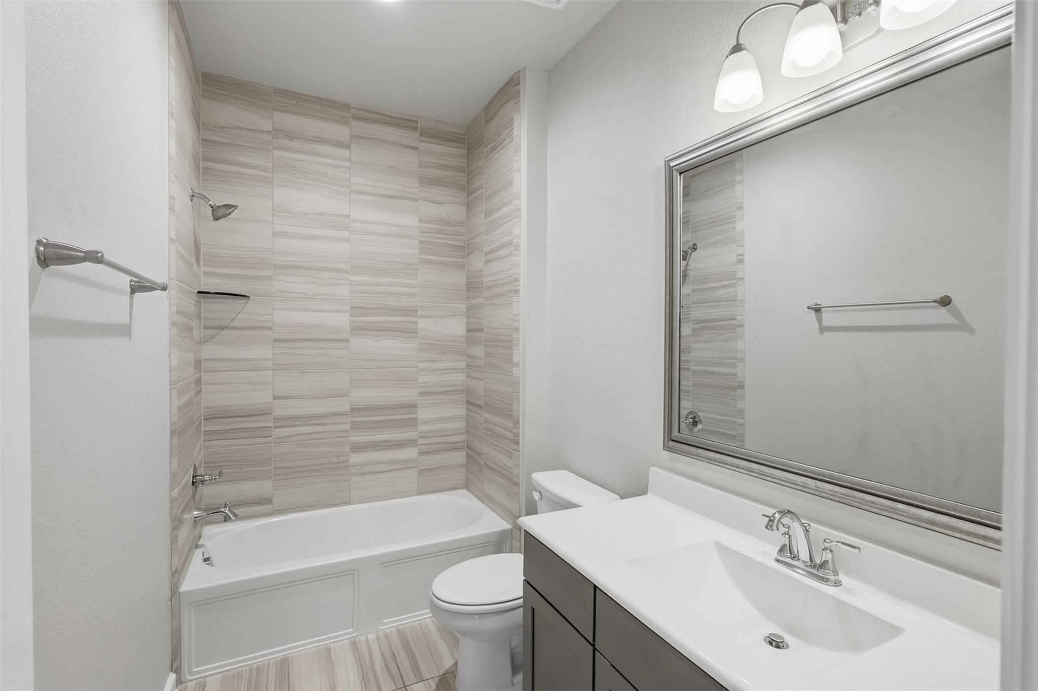 Bathroom with a tiled tub and shower beside a dark vanity and large framed mirror.