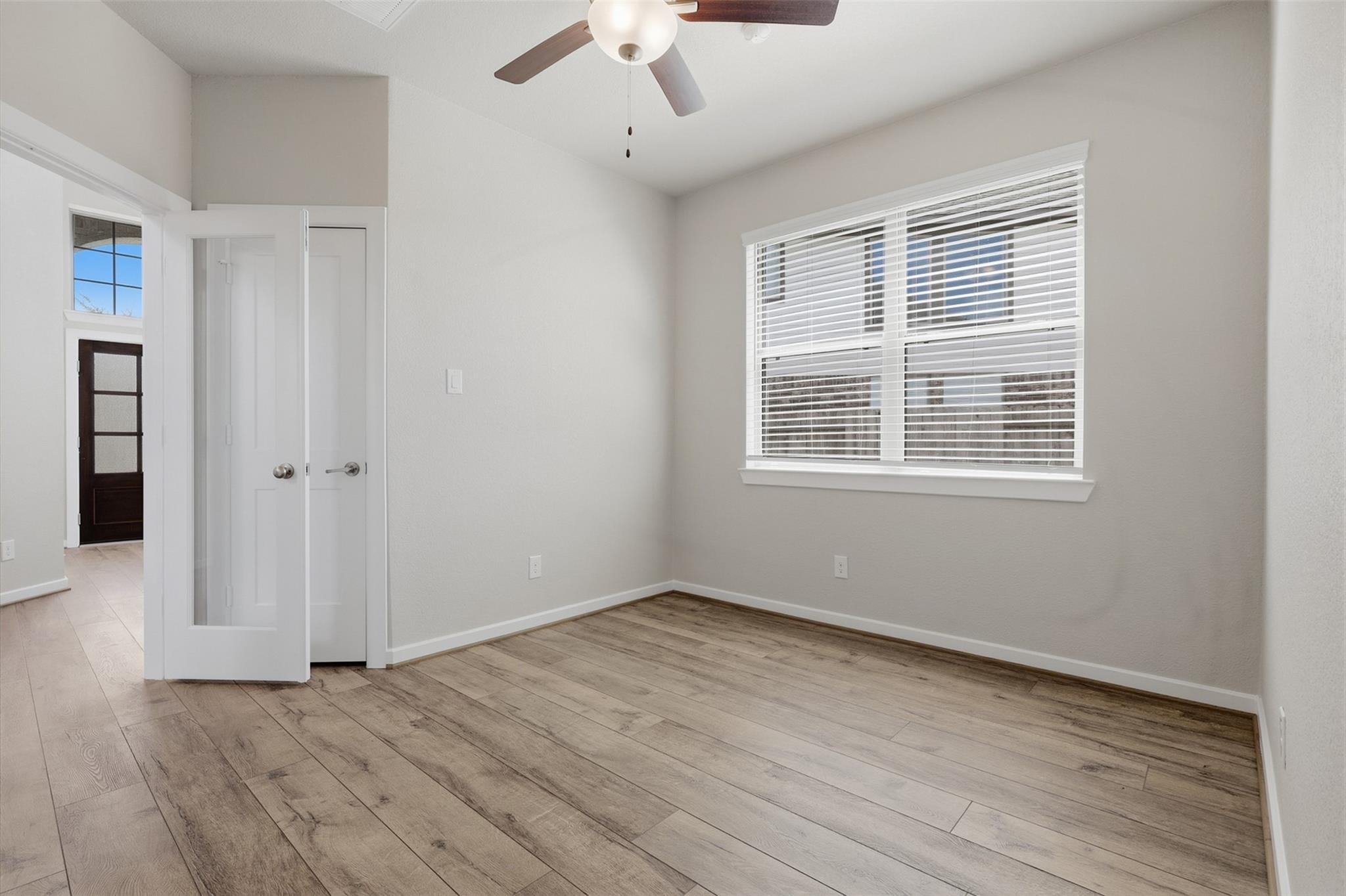 Empty bedroom with wood-look flooring, ceiling fan, and wide window with blinds.