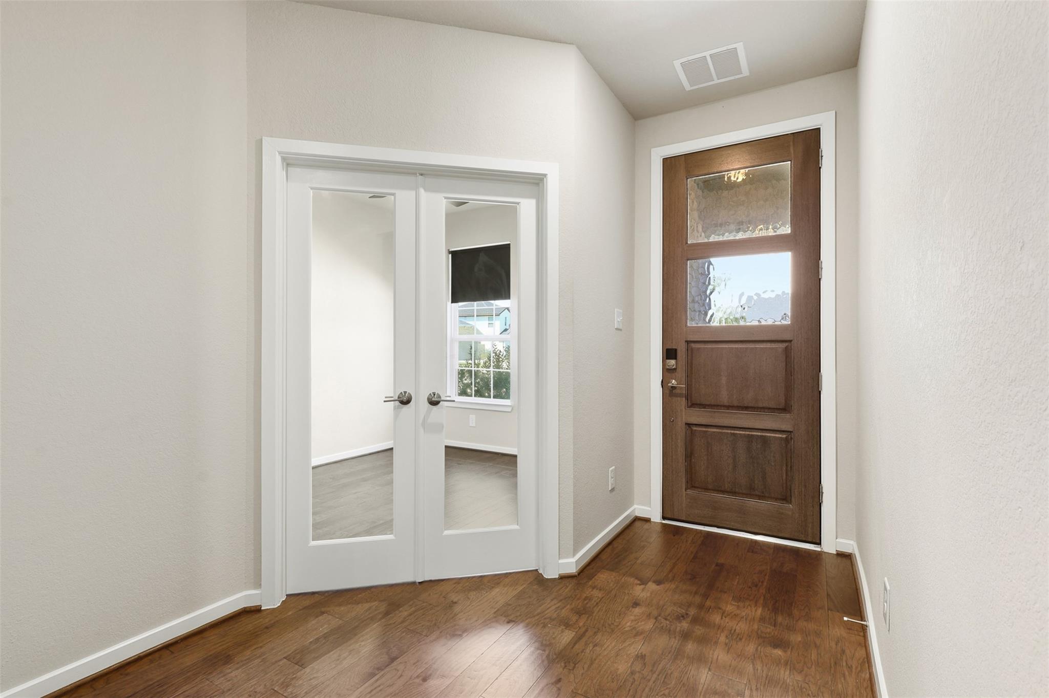 Entryway with a glass-panel wood front door, hardwood floors, and white double doors to a bright room.