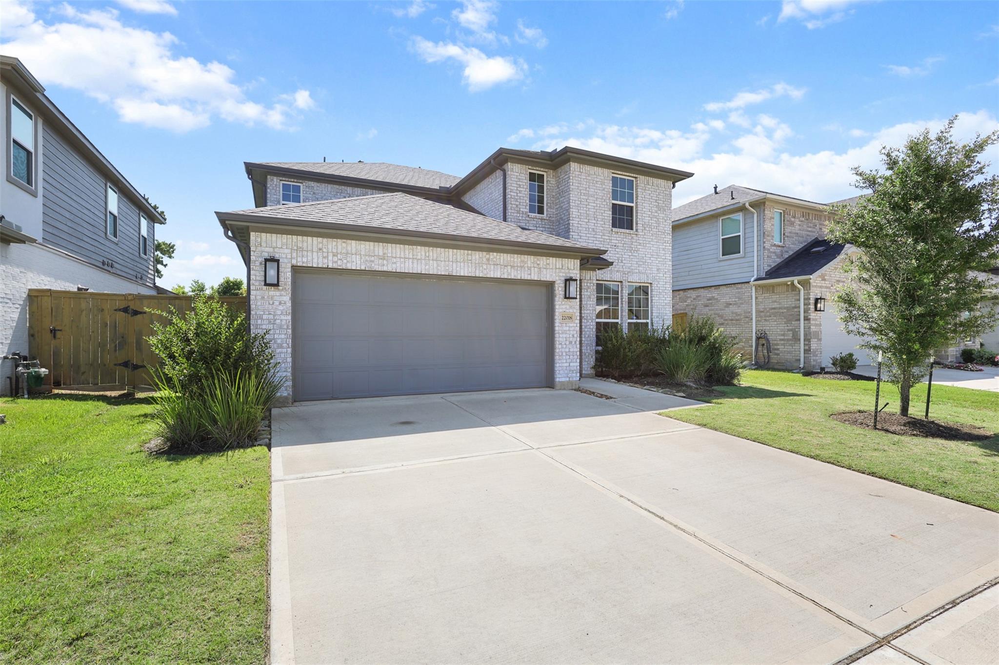 Two-story brick home with a gray double garage and broad concrete driveway.