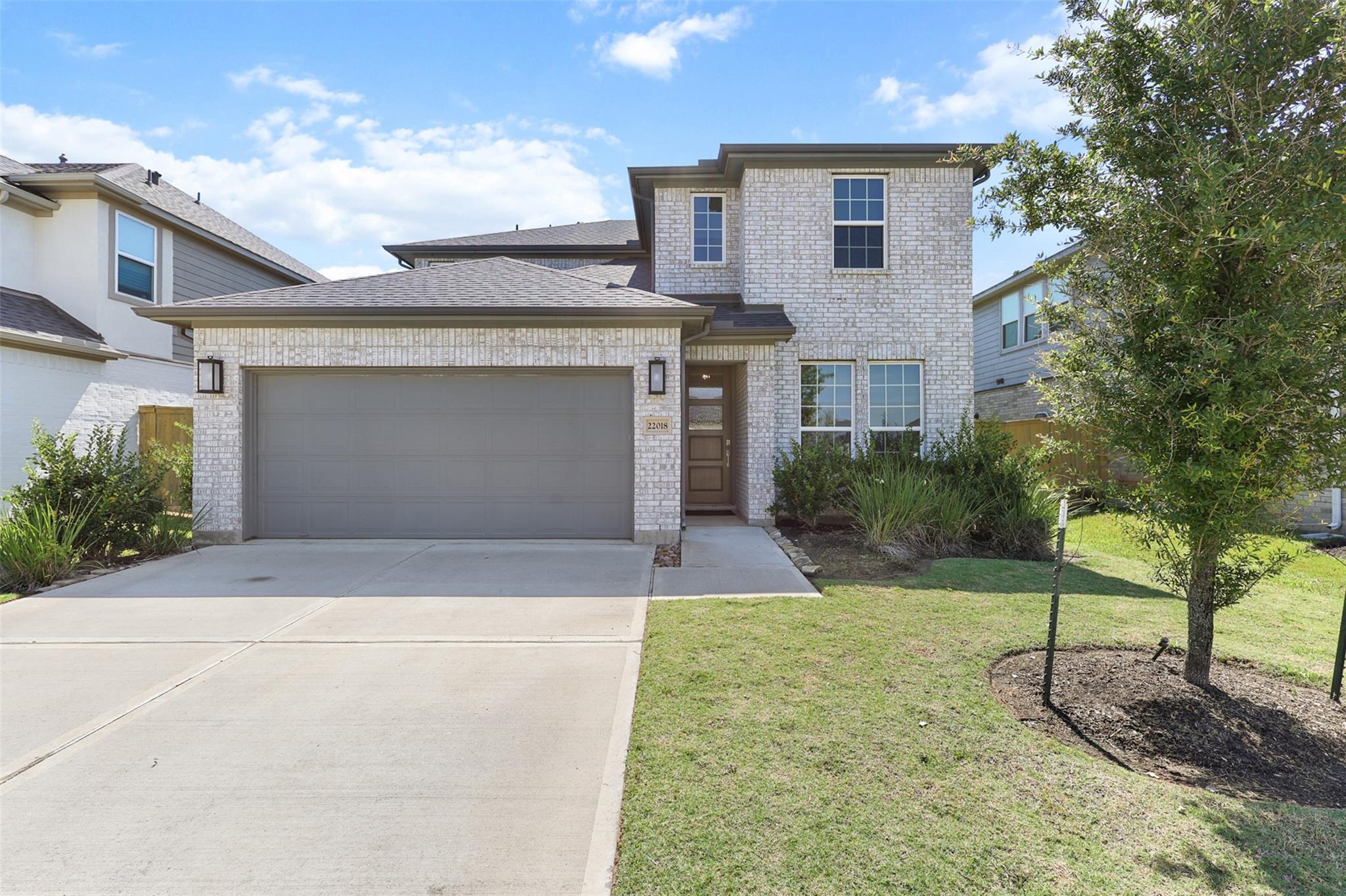 Two-story brick home with a wide garage, landscaped lawn, and driveway.