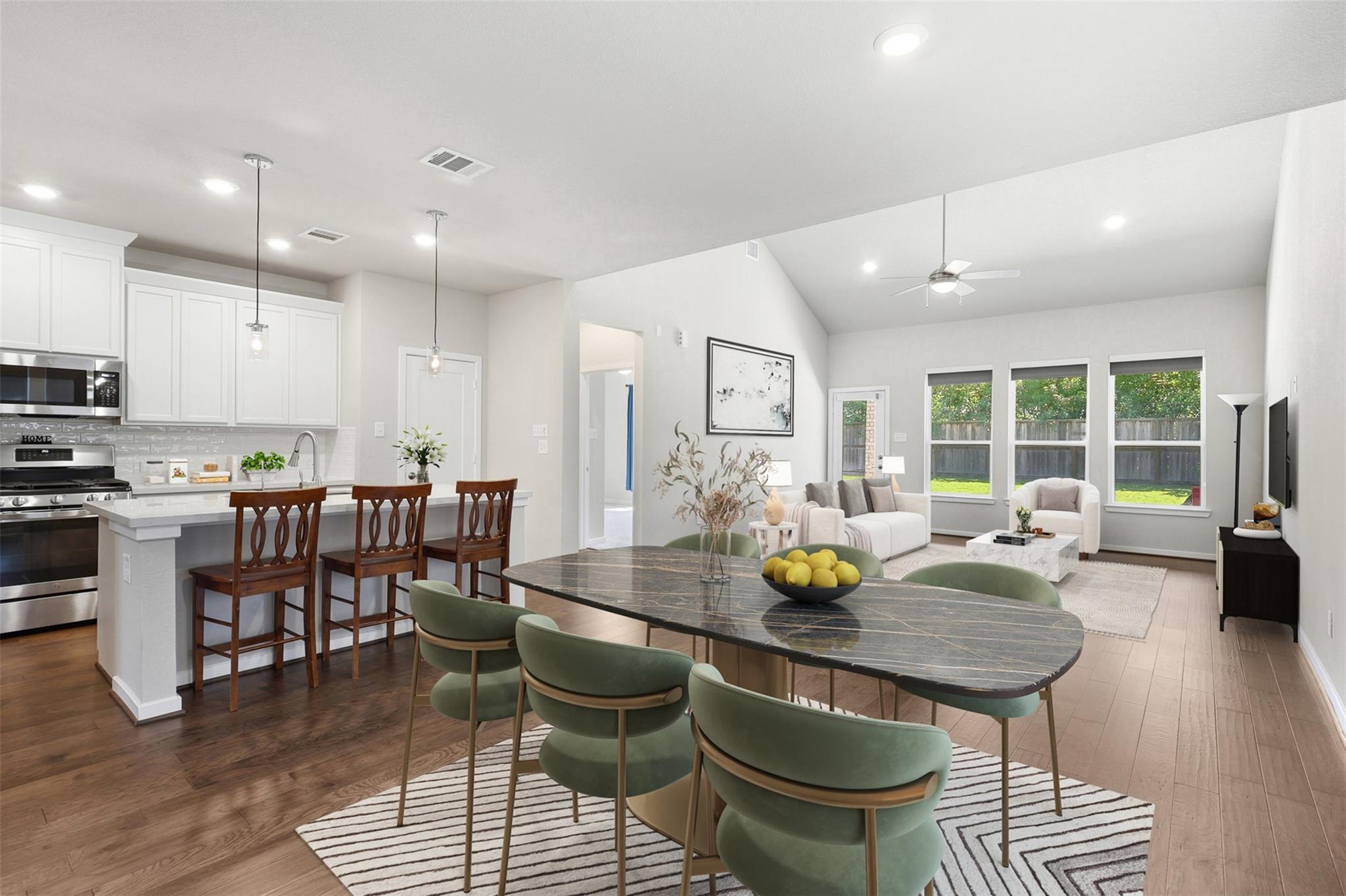 Open-plan kitchen and living area with white cabinetry, a dark dining table, and green chairs.