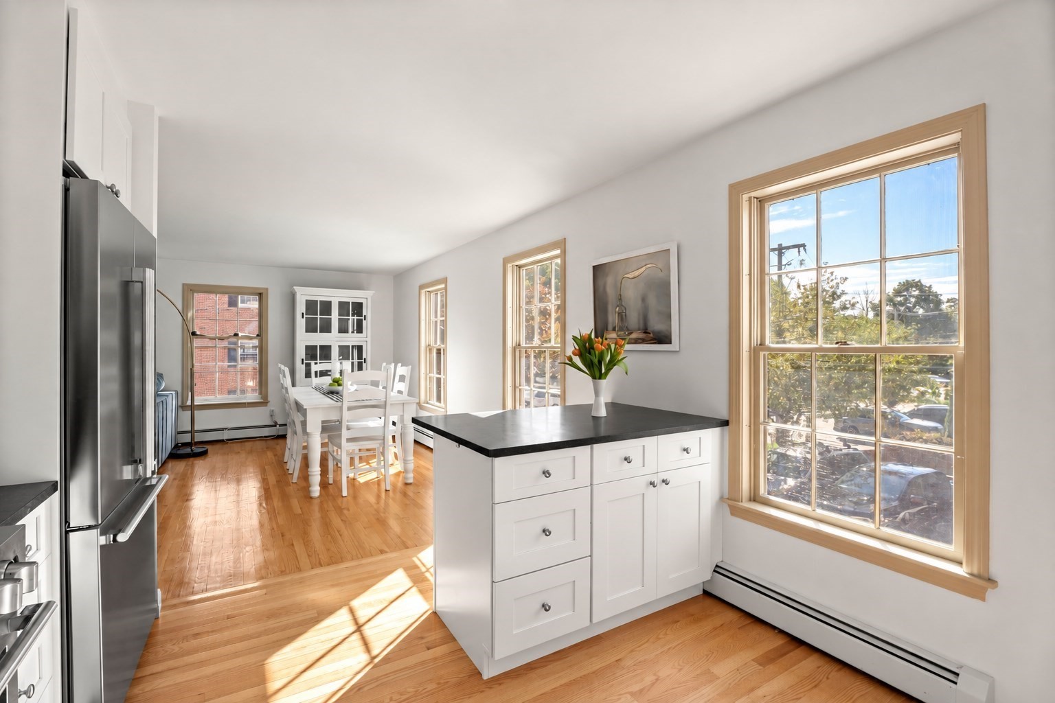 Bright kitchen with a black island, hardwood floors, and a dining table beside tall windows.