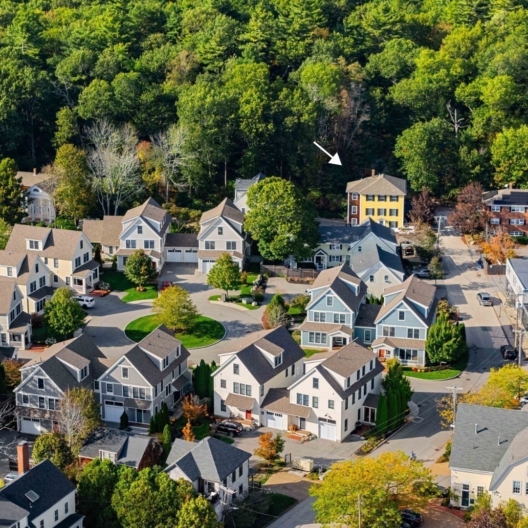 Aerial view of a neighborhood, with an arrow pointing to a yellow multi-story home beside the woods.