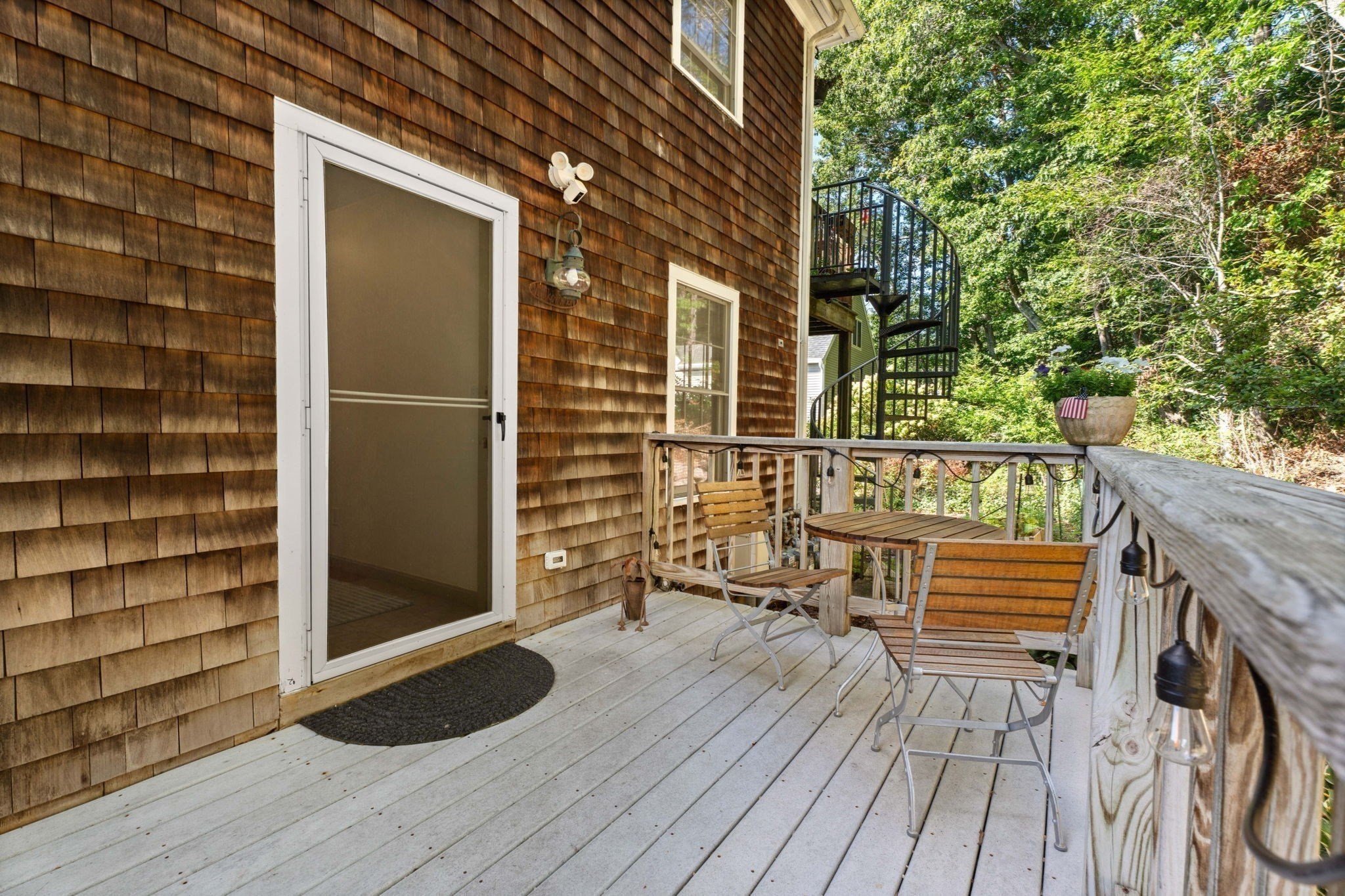 Wooden deck with outdoor seating beside a shingle-sided home and black spiral staircase.