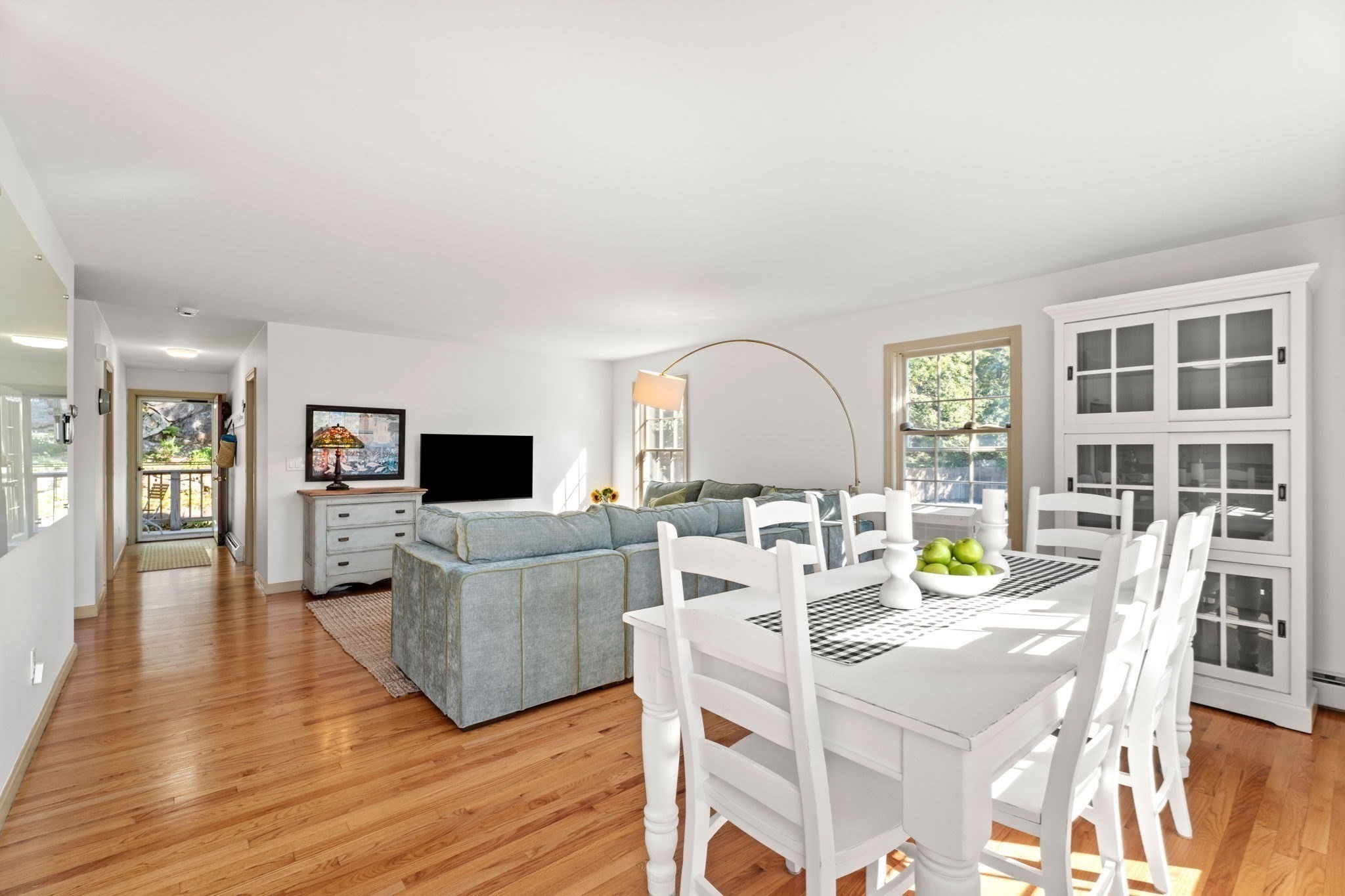 Open-plan living and dining room with hardwood floors, a gray sectional, and a white dining table.