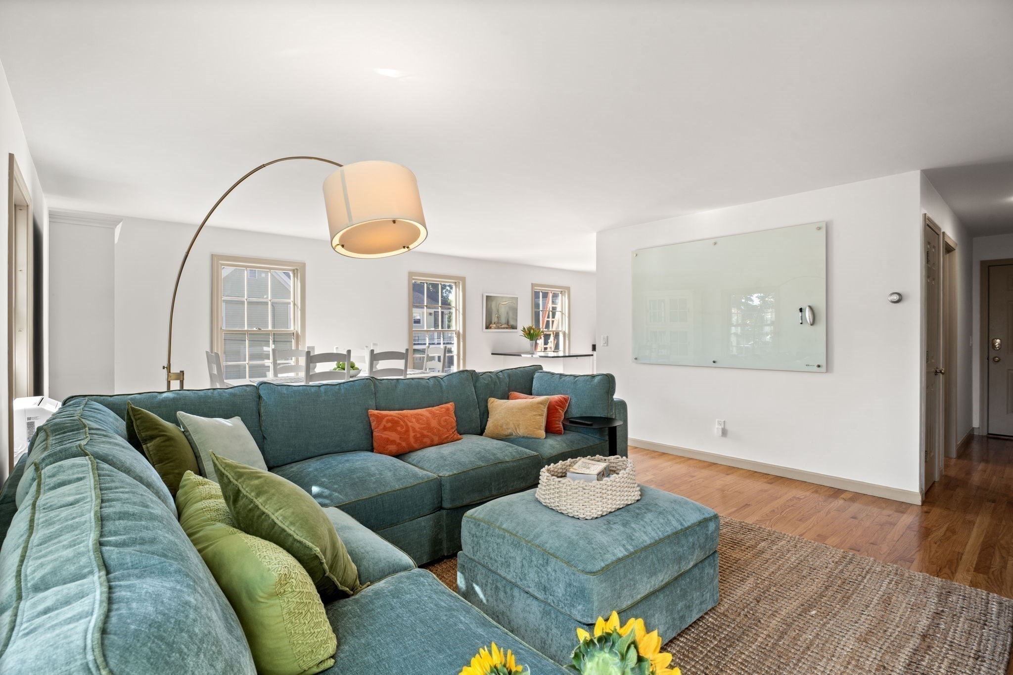Living room with a teal sectional sofa and ottoman, opening onto a bright dining area.