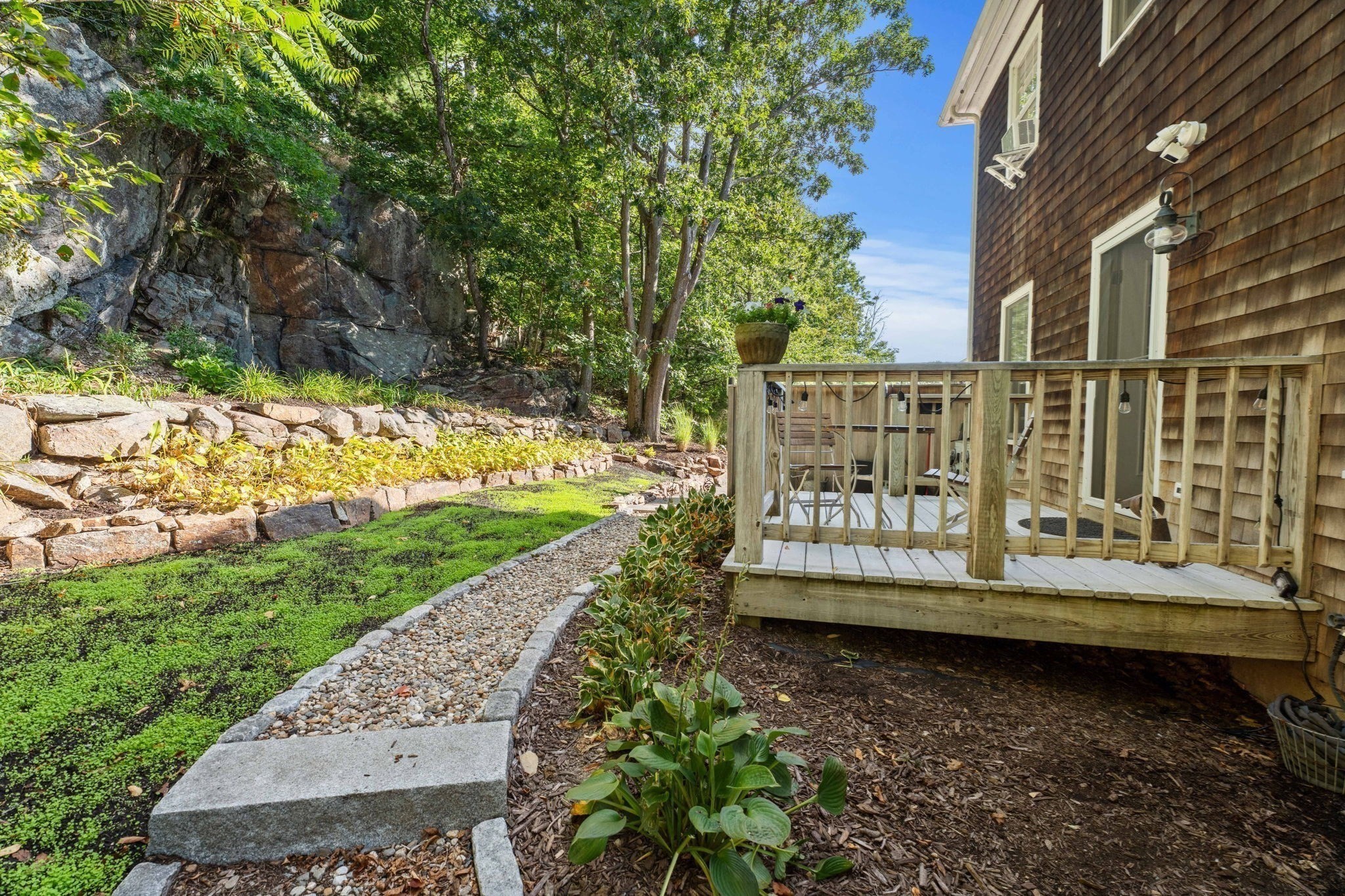 Landscaped garden beside a shingle-sided home, with a raised deck and curved gravel path.