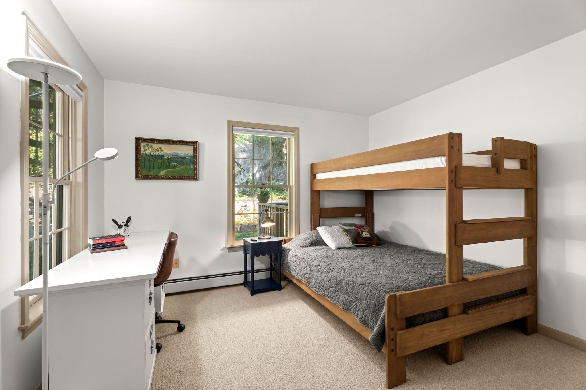 Bedroom with a wooden bunk bed and white desk beside tall windows.