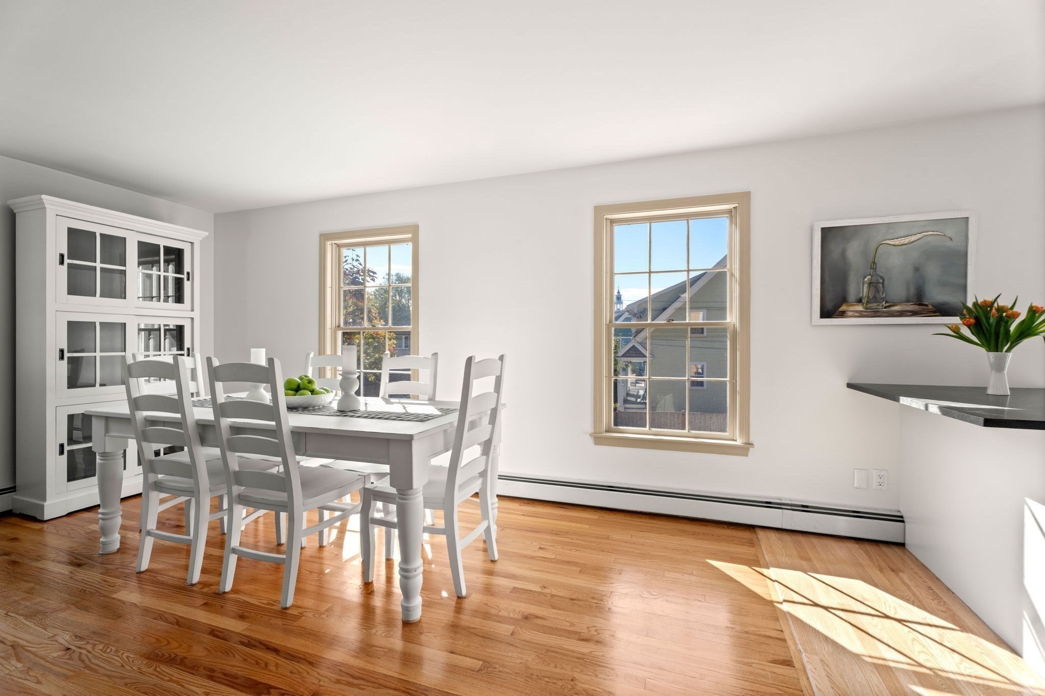 Dining room with a white table, glass-front cabinet, and sunlit hardwood floors.